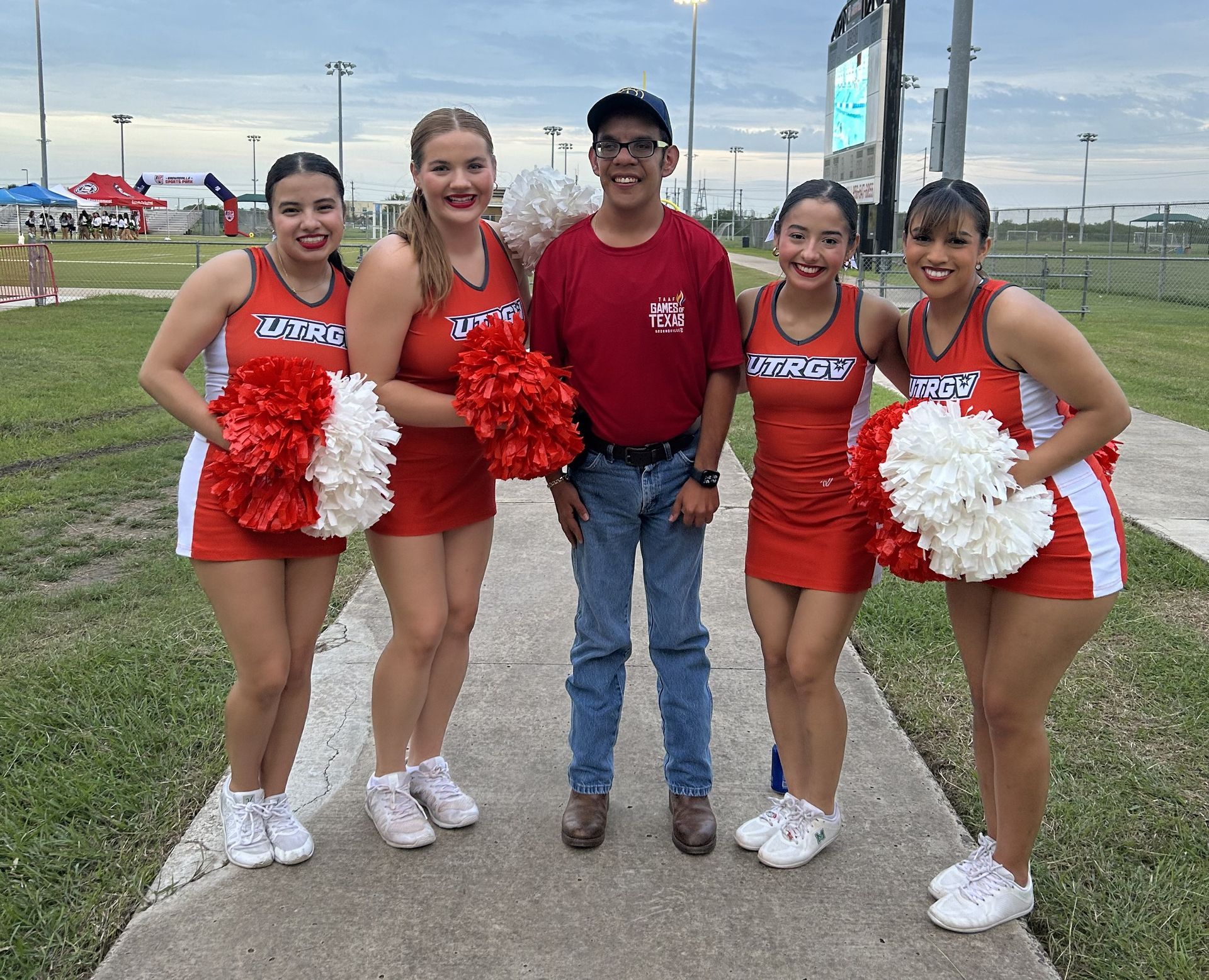 A group of cheerleaders are posing for a picture with a man.