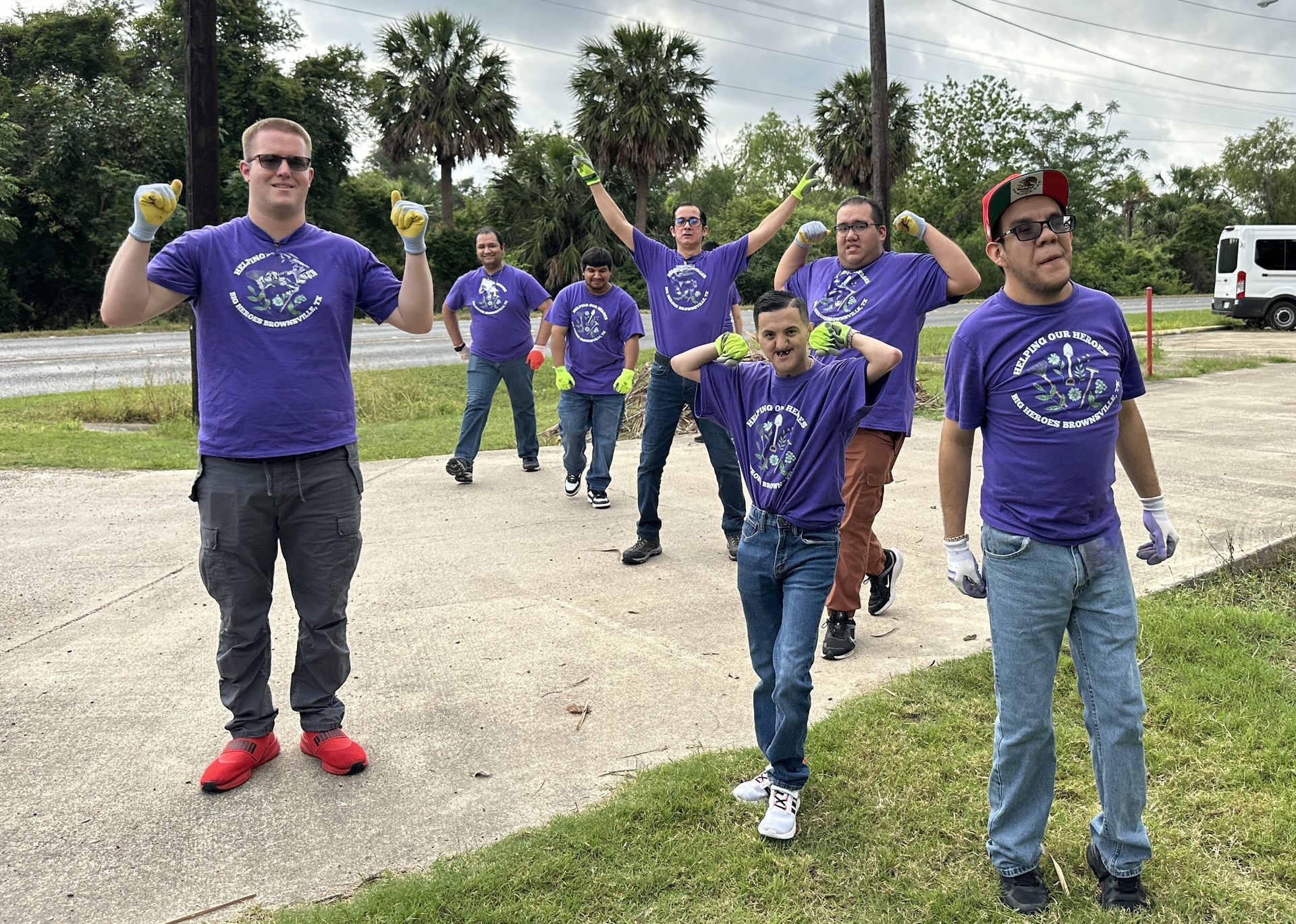 A group of men in purple shirts are standing next to each other on a sidewalk.