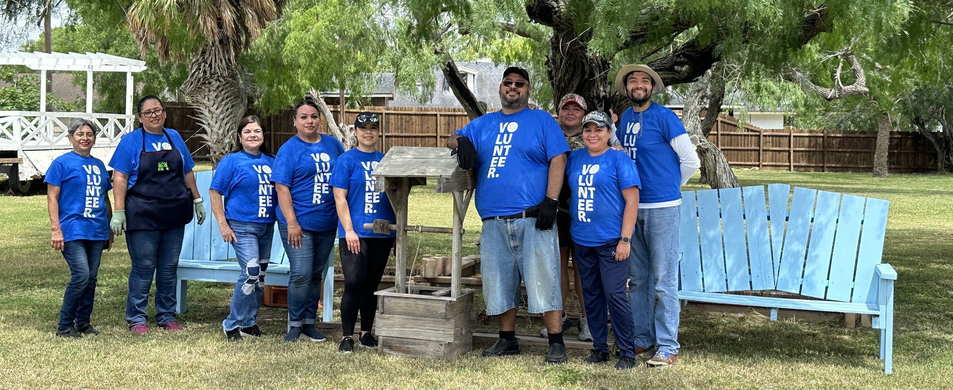 A group of people in blue shirts are standing next to blue benches in a park.