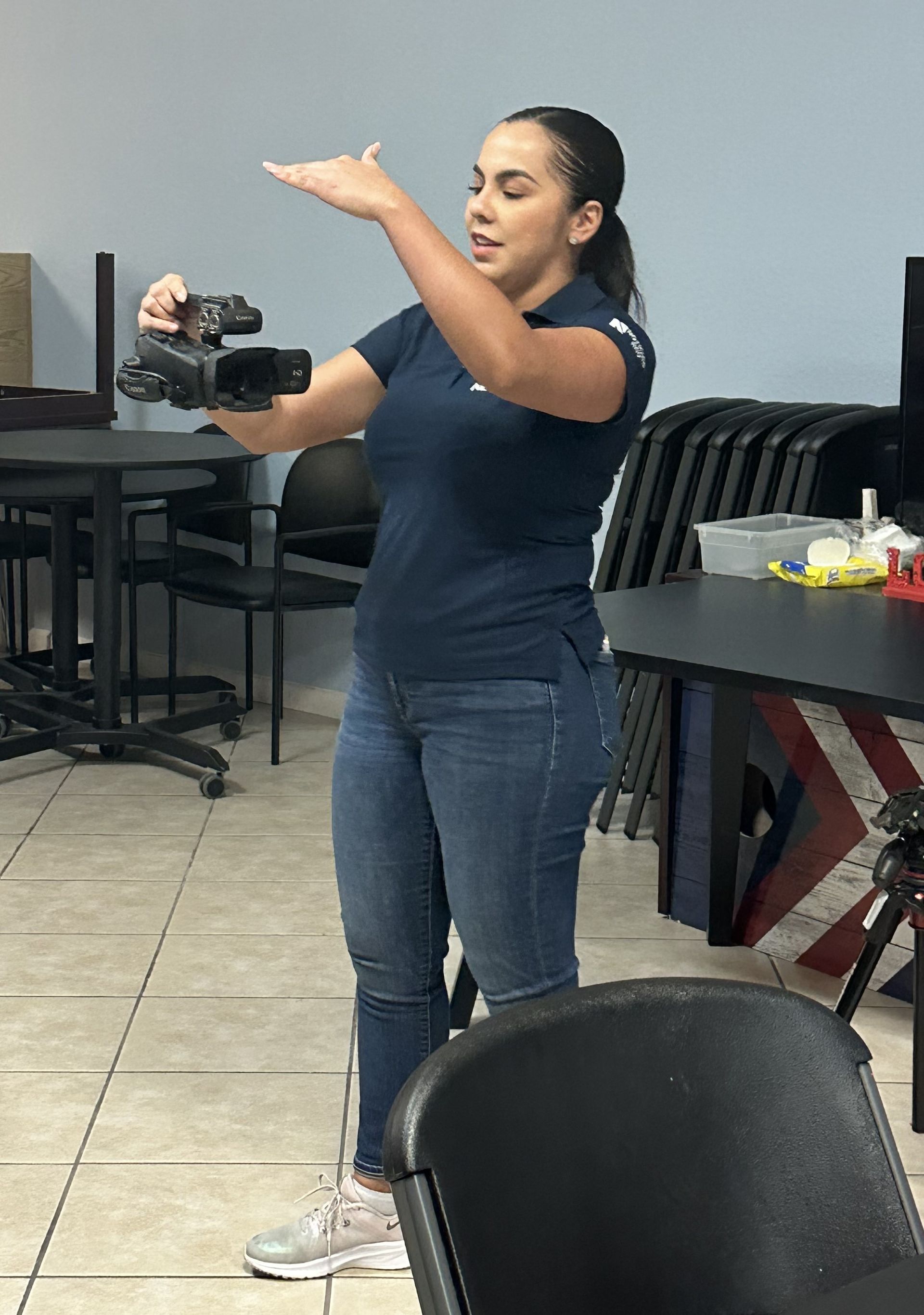 A woman in a blue shirt is holding a camera in a room.