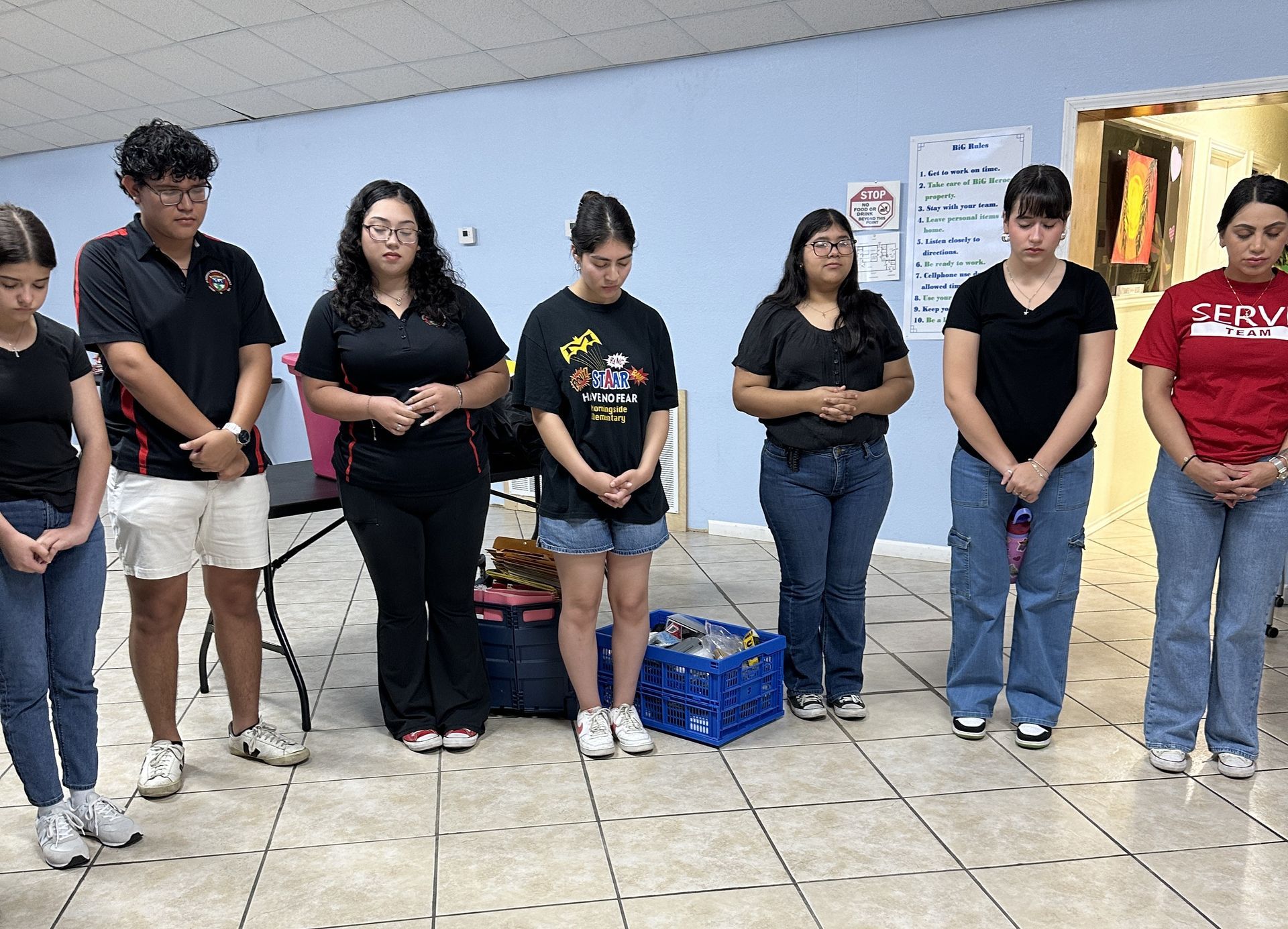 A group of people are standing in a room with their hands folded