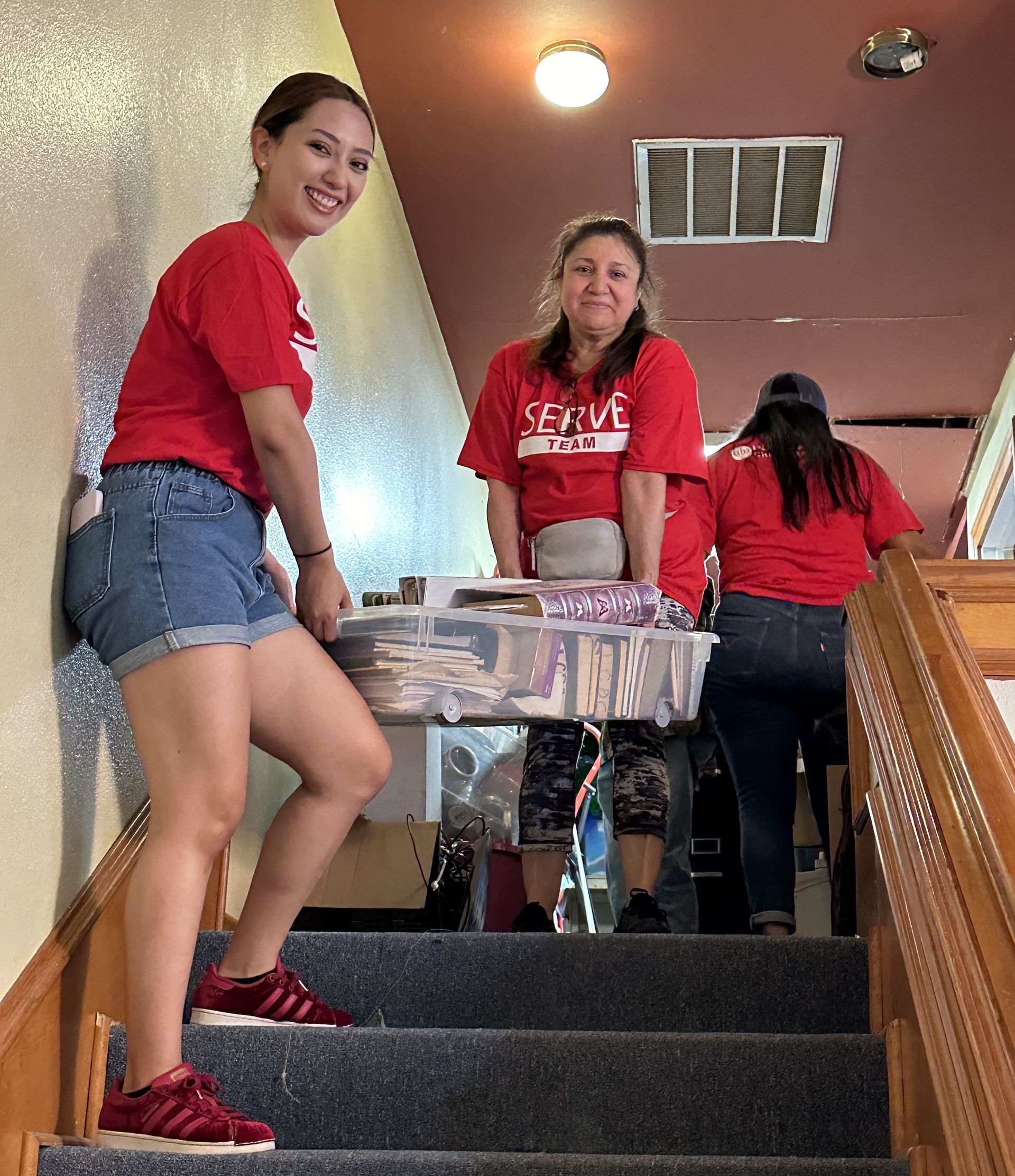 A woman in a red shirt is standing on a set of stairs holding a box.
