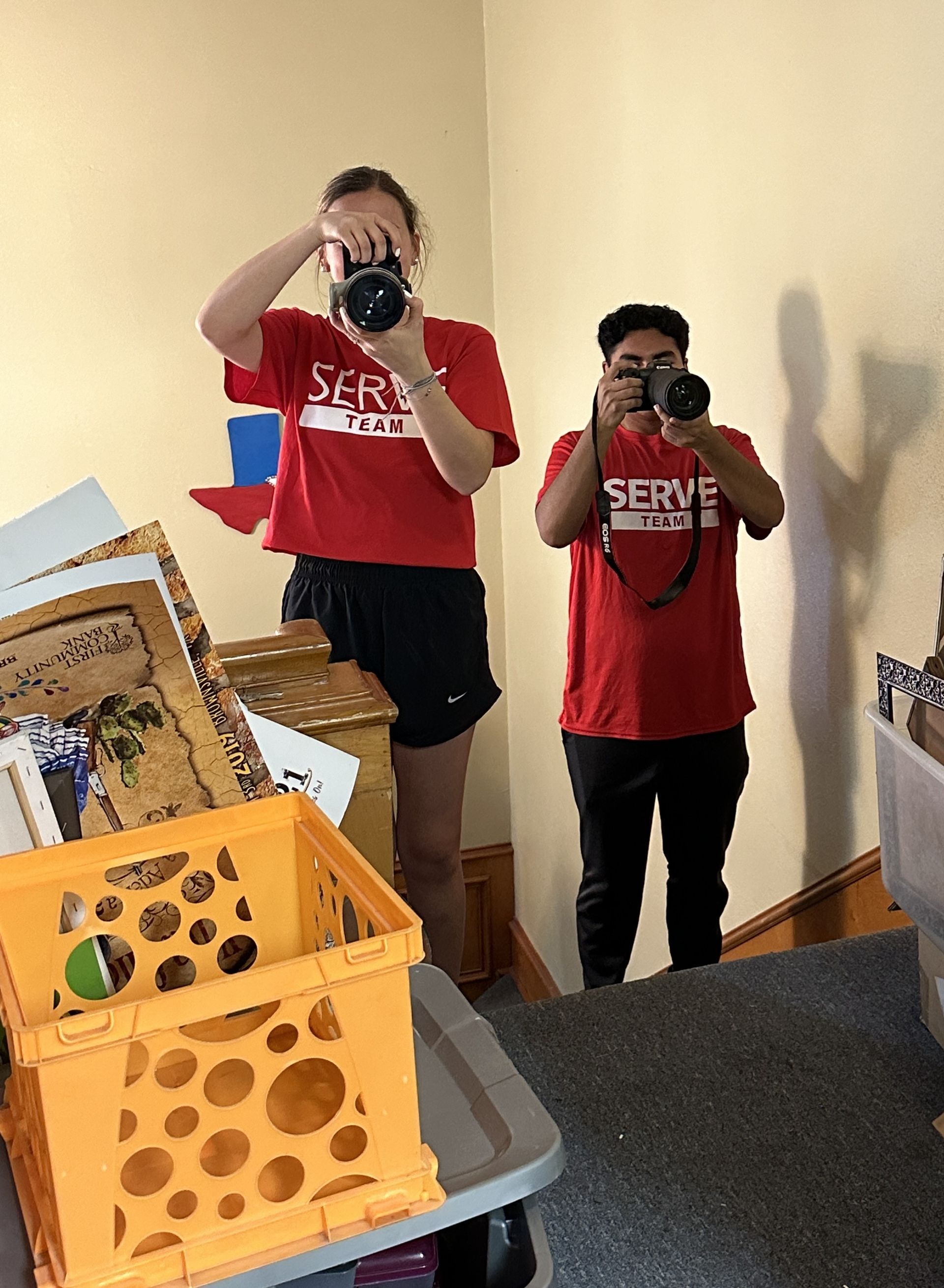Two people in red shirts are taking pictures of themselves in a mirror.