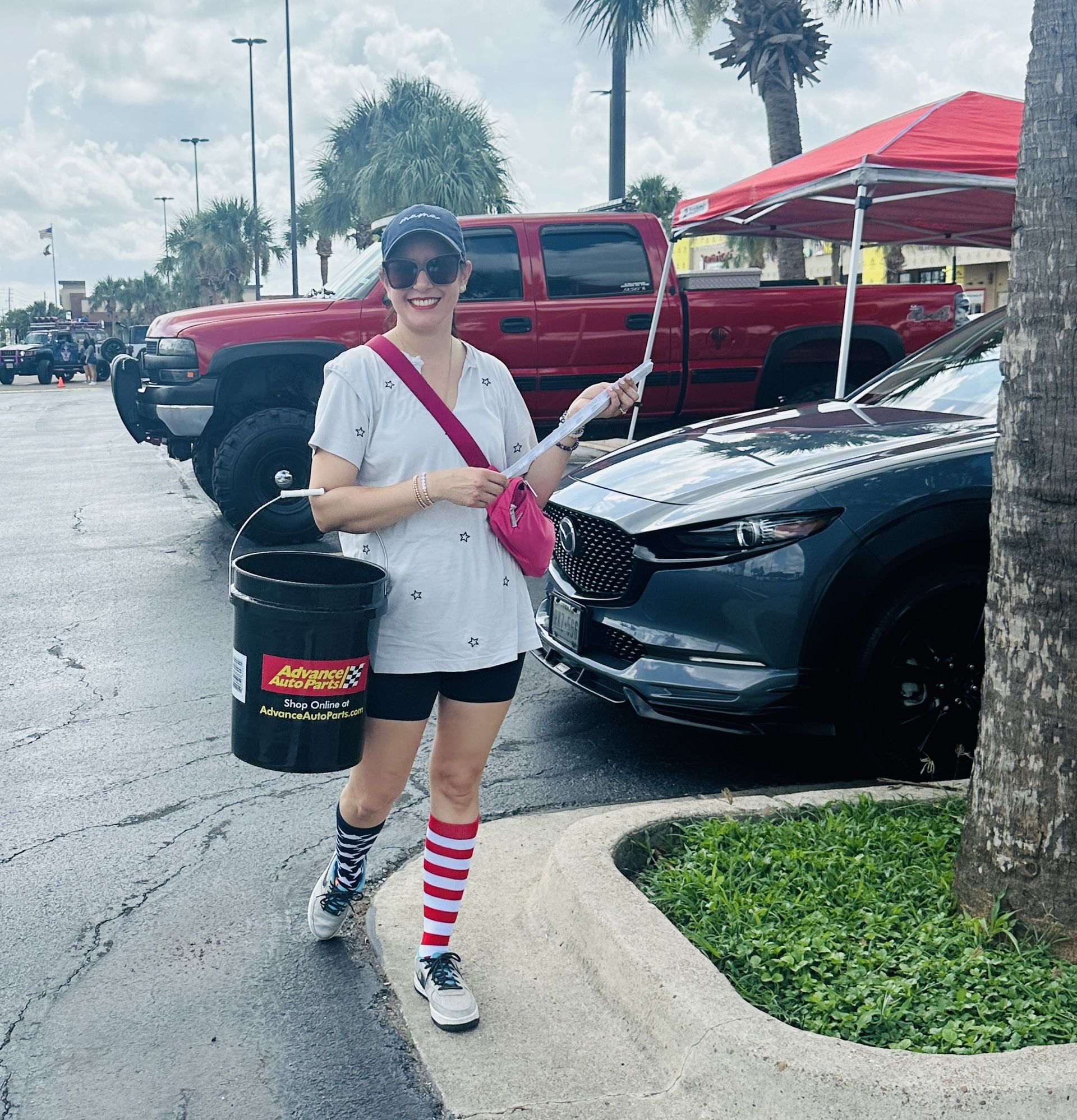 A woman is standing in front of a car holding a bucket that says ' jeep ' on it