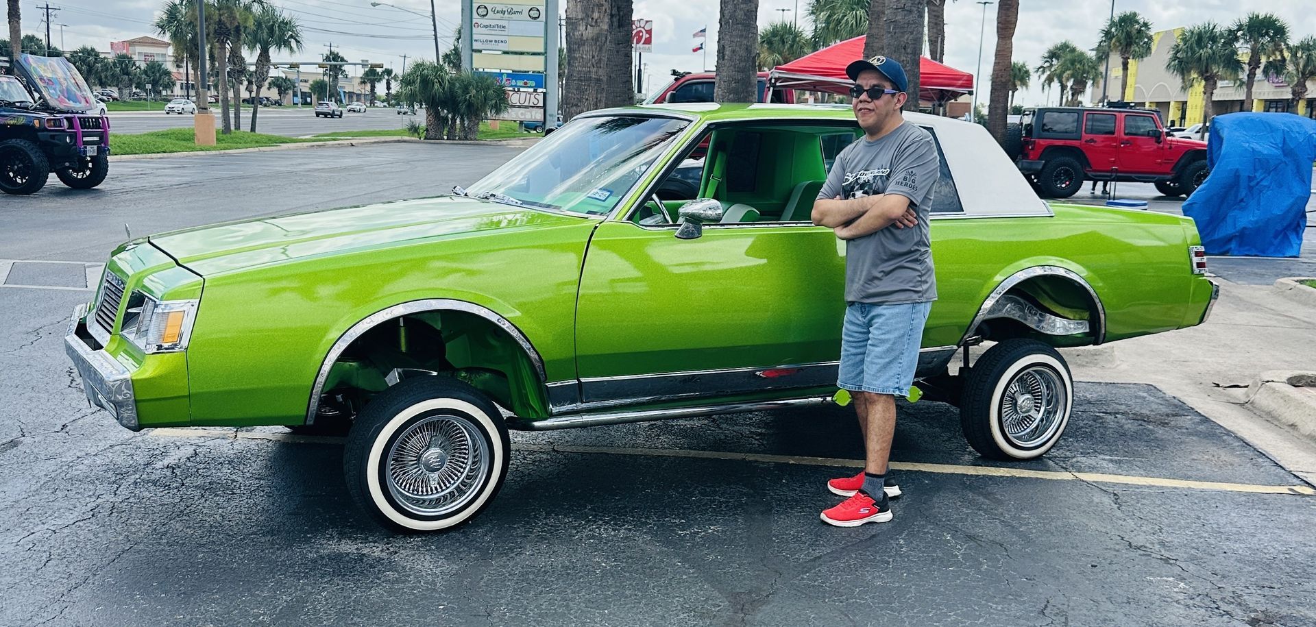 A man is standing next to a green car in a parking lot.