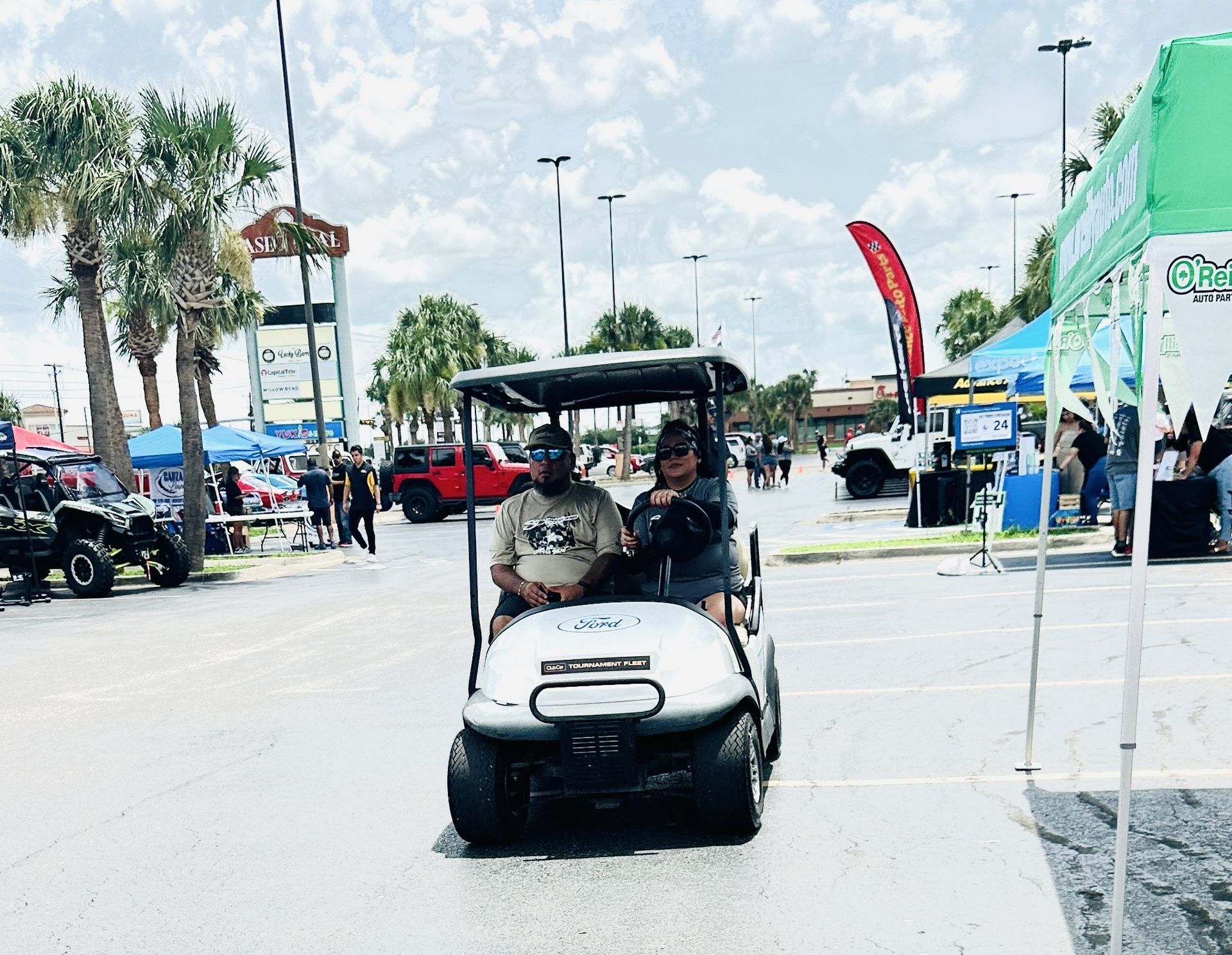 Two men are riding a golf cart in a parking lot.