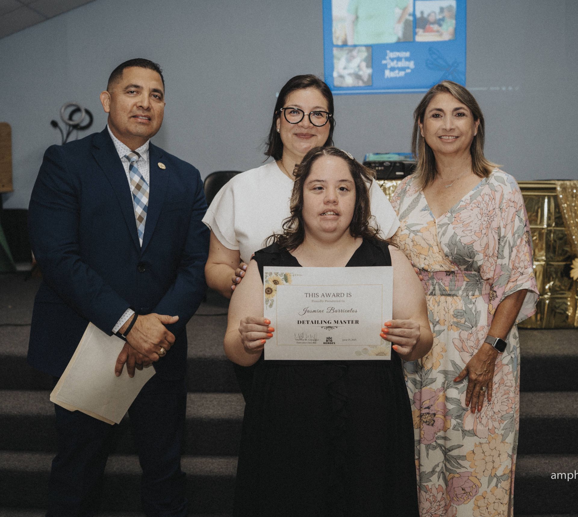 Group of four people, smiling, with a certificate. Woman in the front holds the certificate; two women and a man flank her.