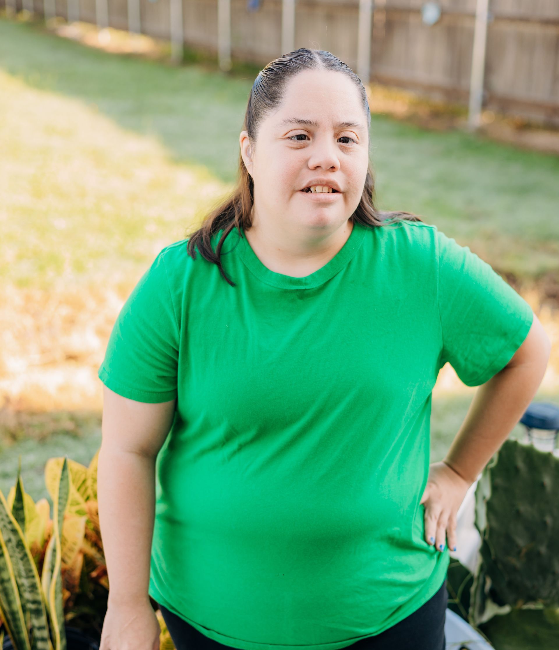 A woman in a green shirt is standing in the grass with her hands on her hips.