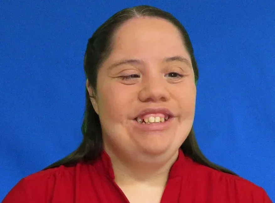 A woman in a red shirt is smiling in front of a blue background.