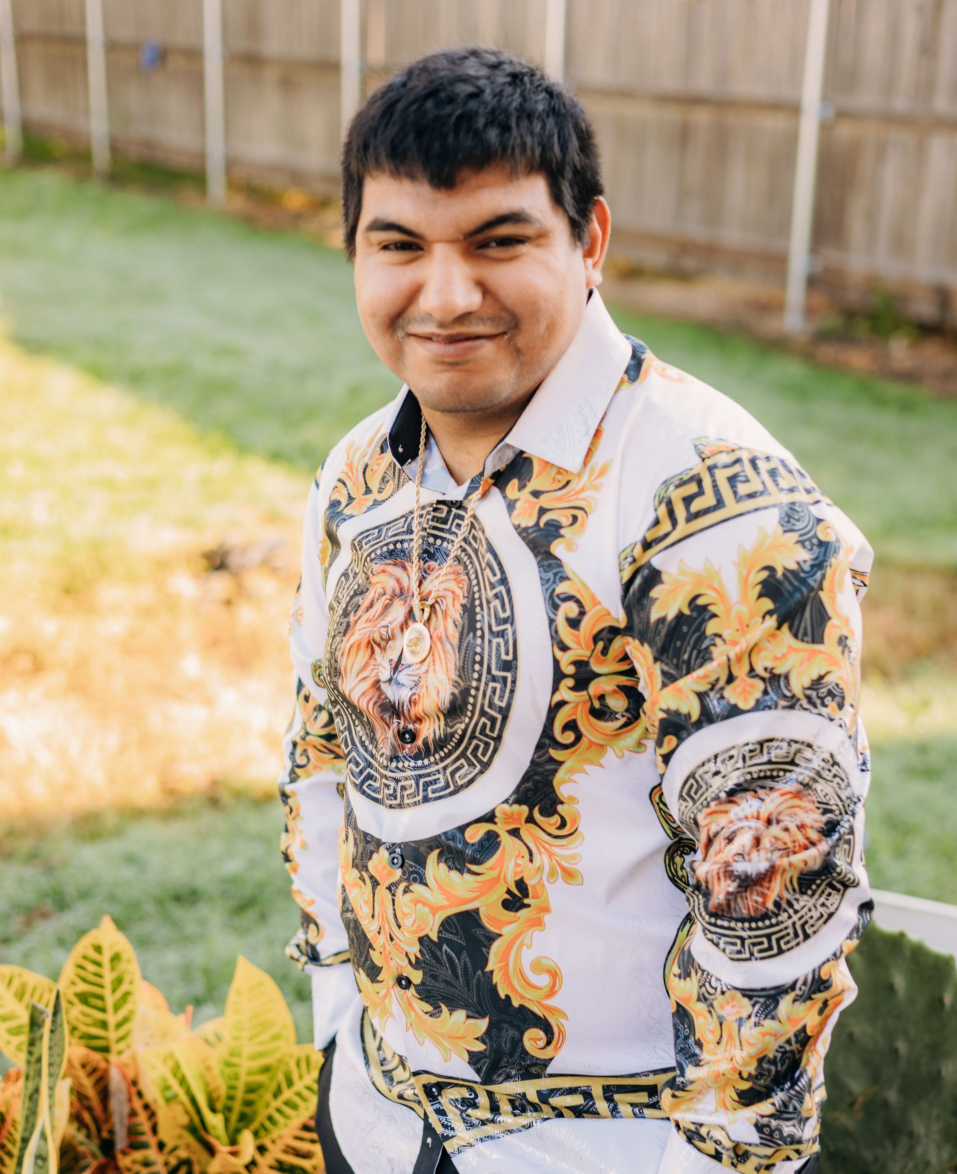 A man wearing a versace shirt is standing in front of a fence.