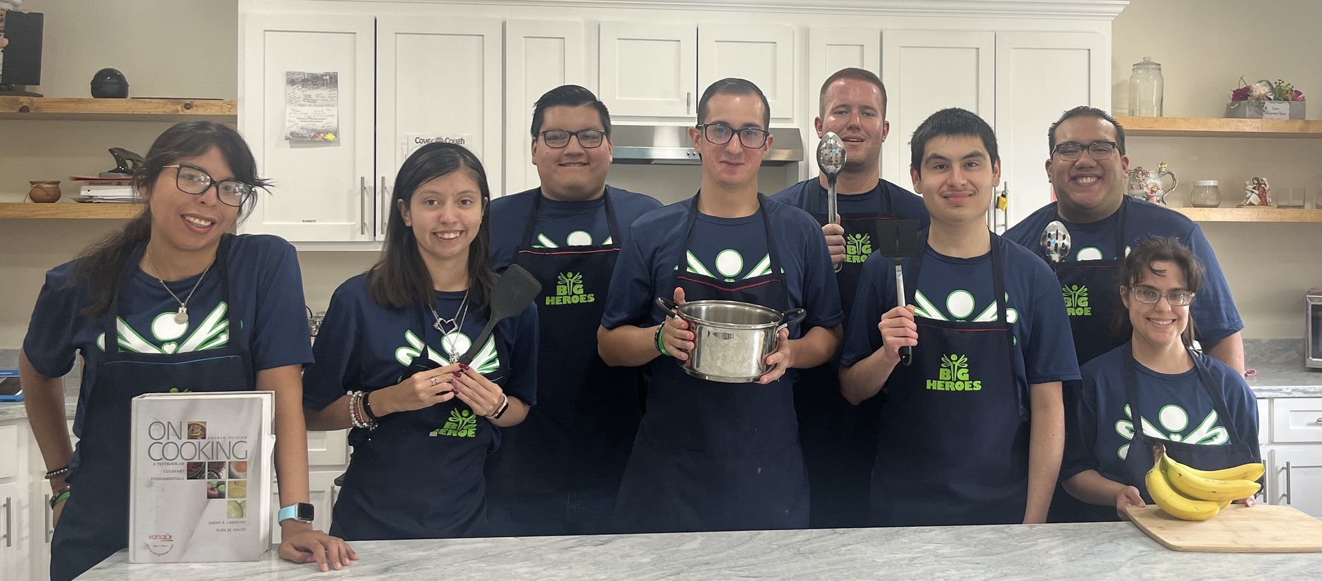 A group of people are standing in a kitchen holding pots and pans.