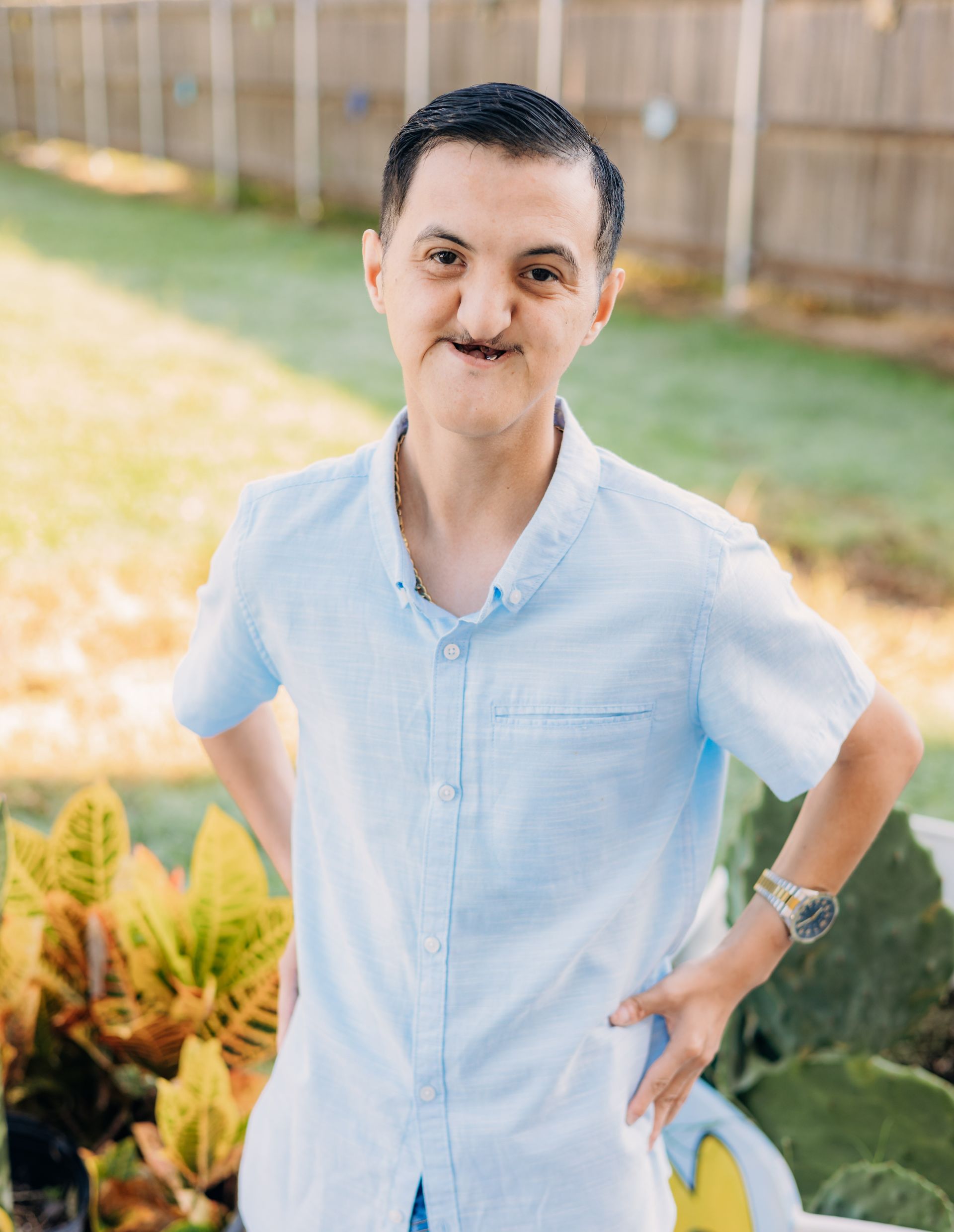 A man with a disability is standing in a garden with his hands on his hips.