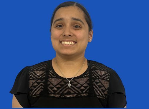 A woman in a black shirt and necklace is smiling against a blue background.