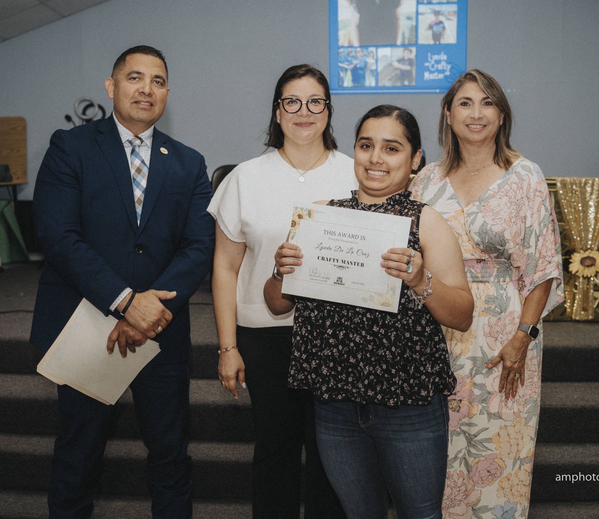 Four people on a stage, a woman holding a certificate smiles.