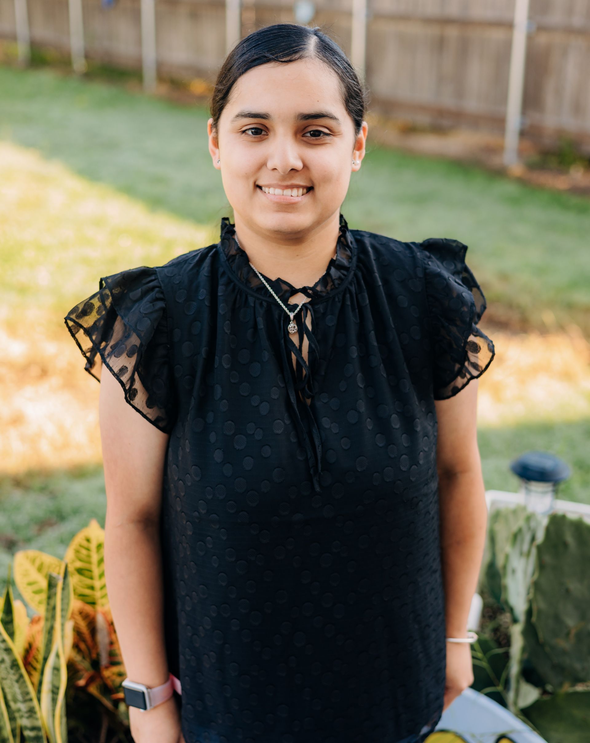A woman in a black shirt is standing in front of a fence.