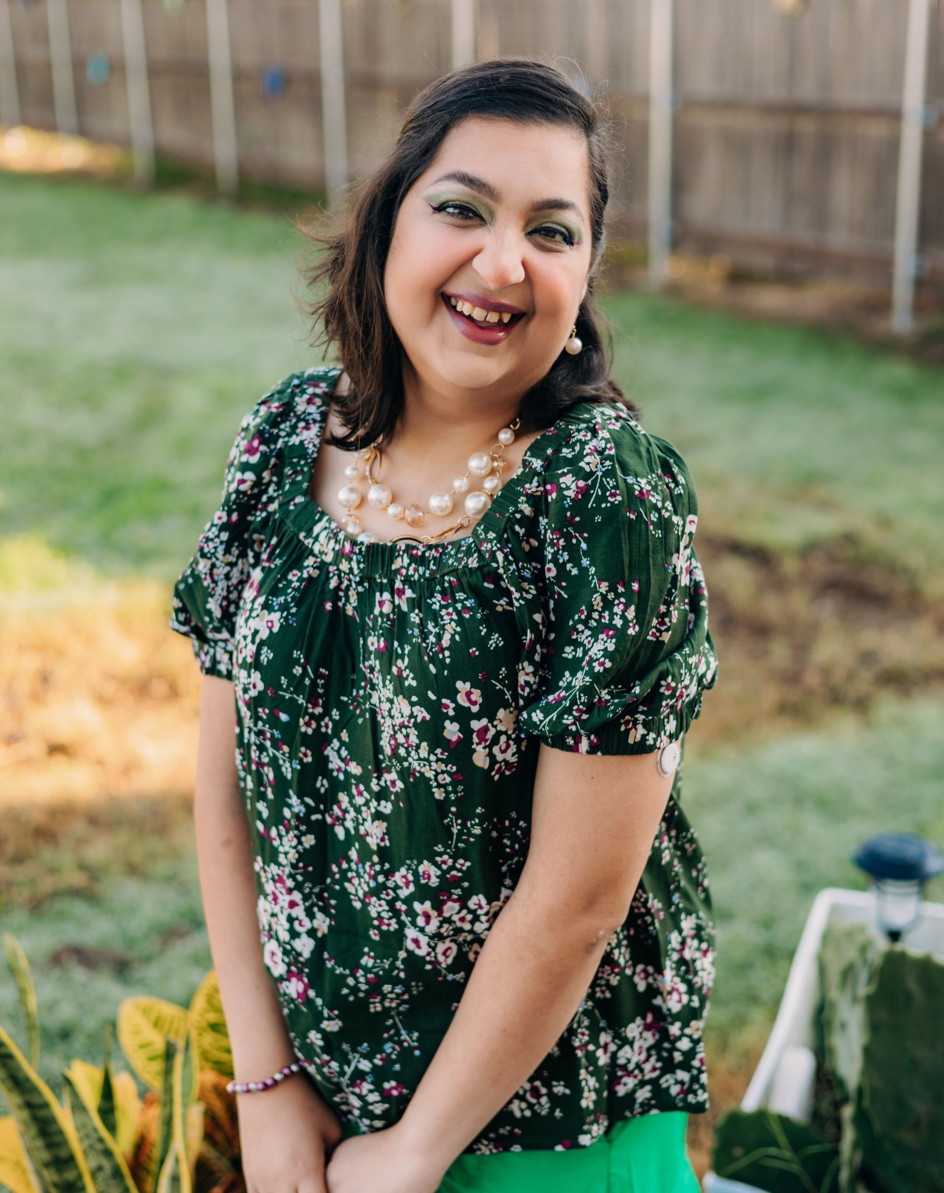 A woman in a green floral top and green pants is smiling.