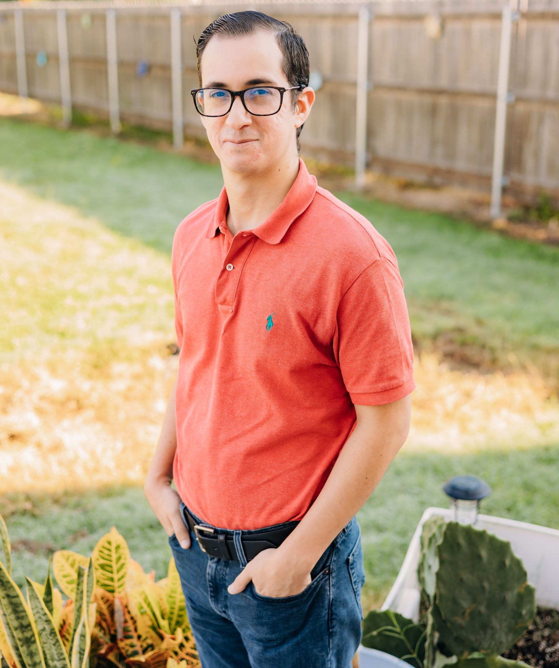 A man wearing glasses and a red shirt is standing in a garden.