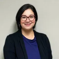 A woman wearing glasses and a black jacket is smiling for the camera.
