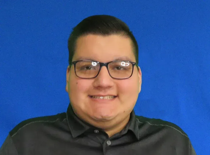 A young man wearing glasses and a black shirt is smiling for the camera.