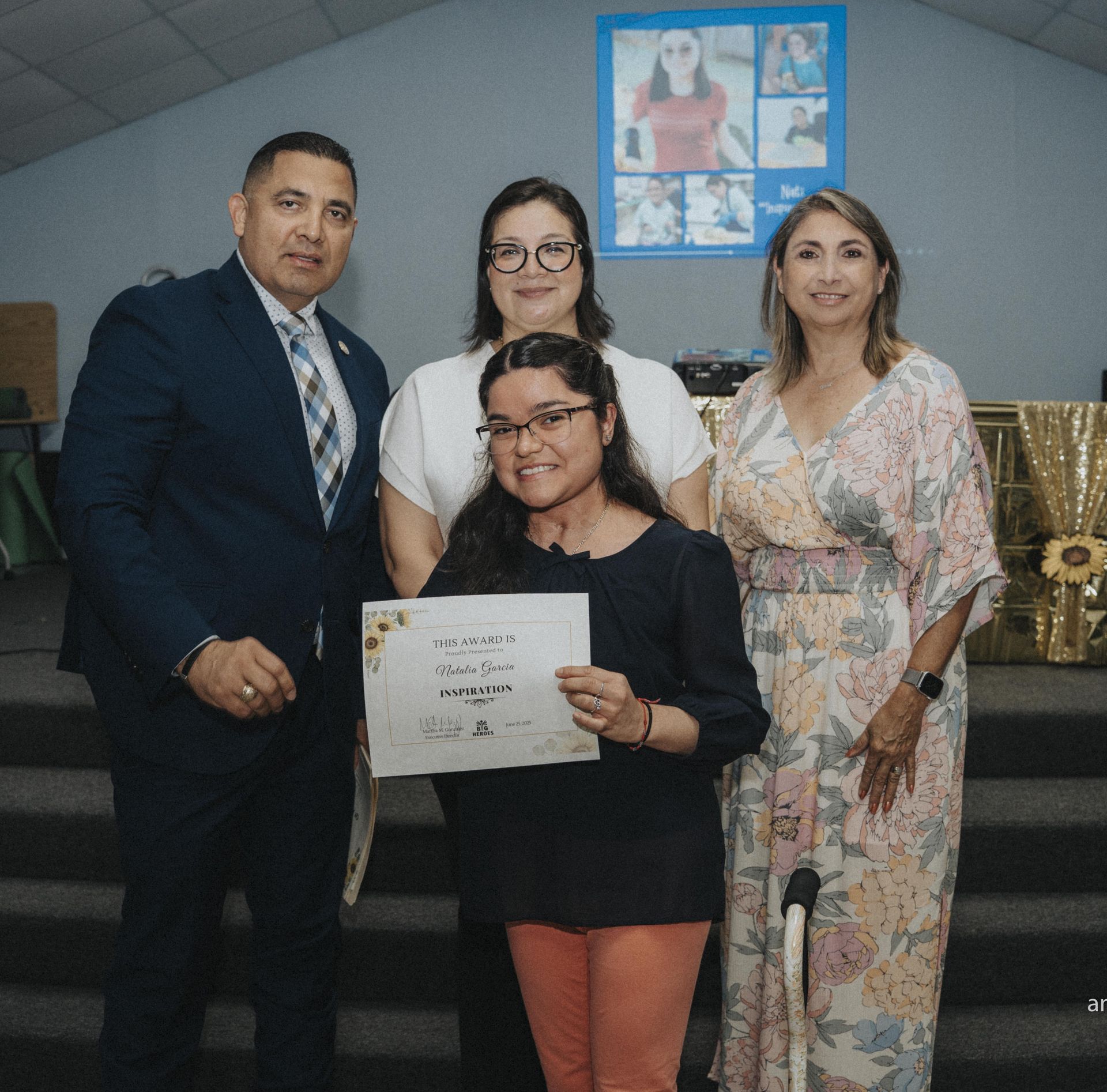 Group of four people, including a young woman holding a certificate. All are smiling inside a building.