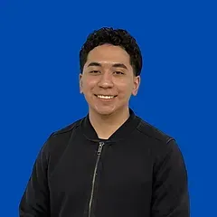A young man in a black jacket is smiling in front of a blue background.