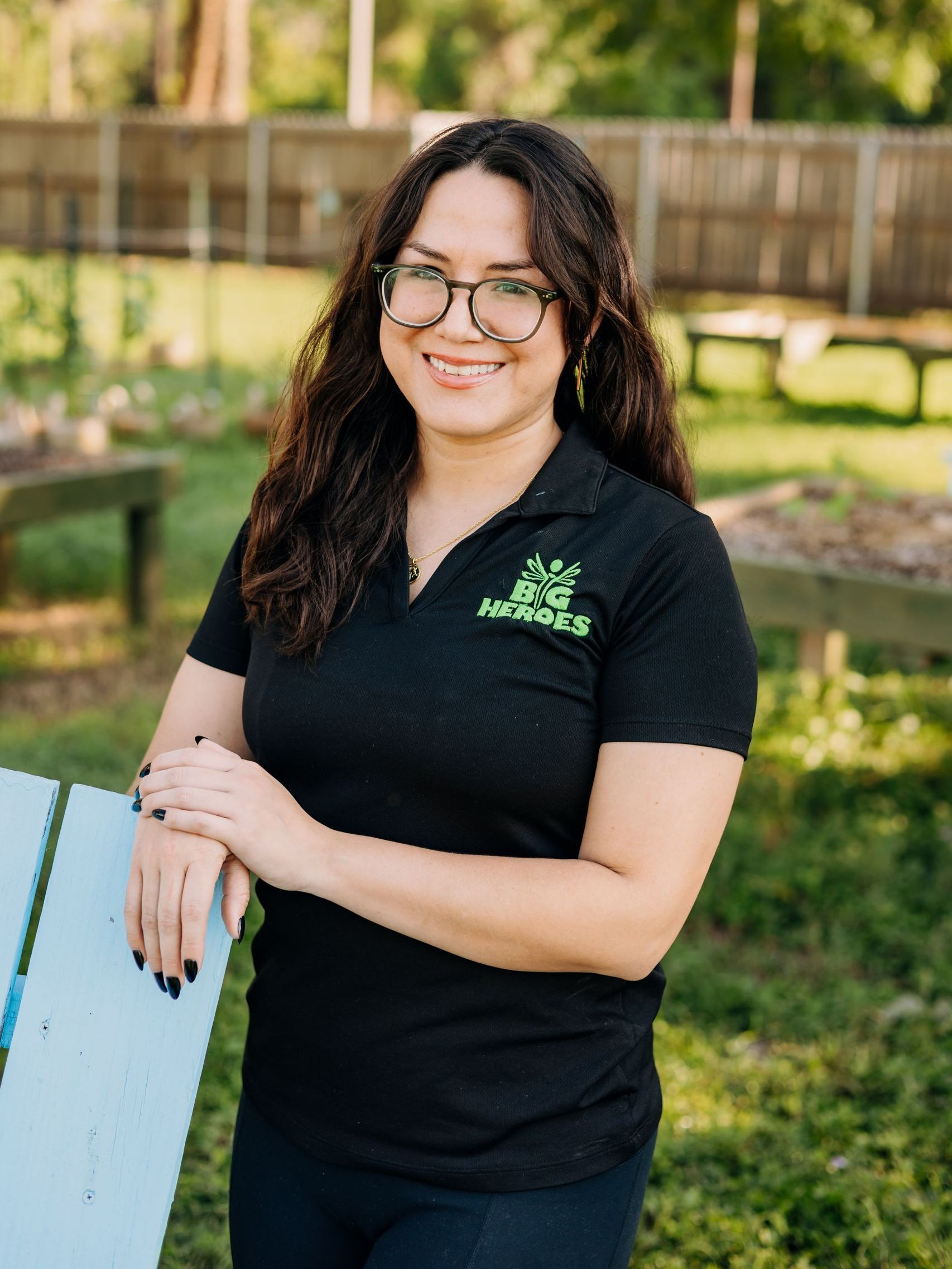 A woman wearing glasses and a black shirt is standing next to a bench.