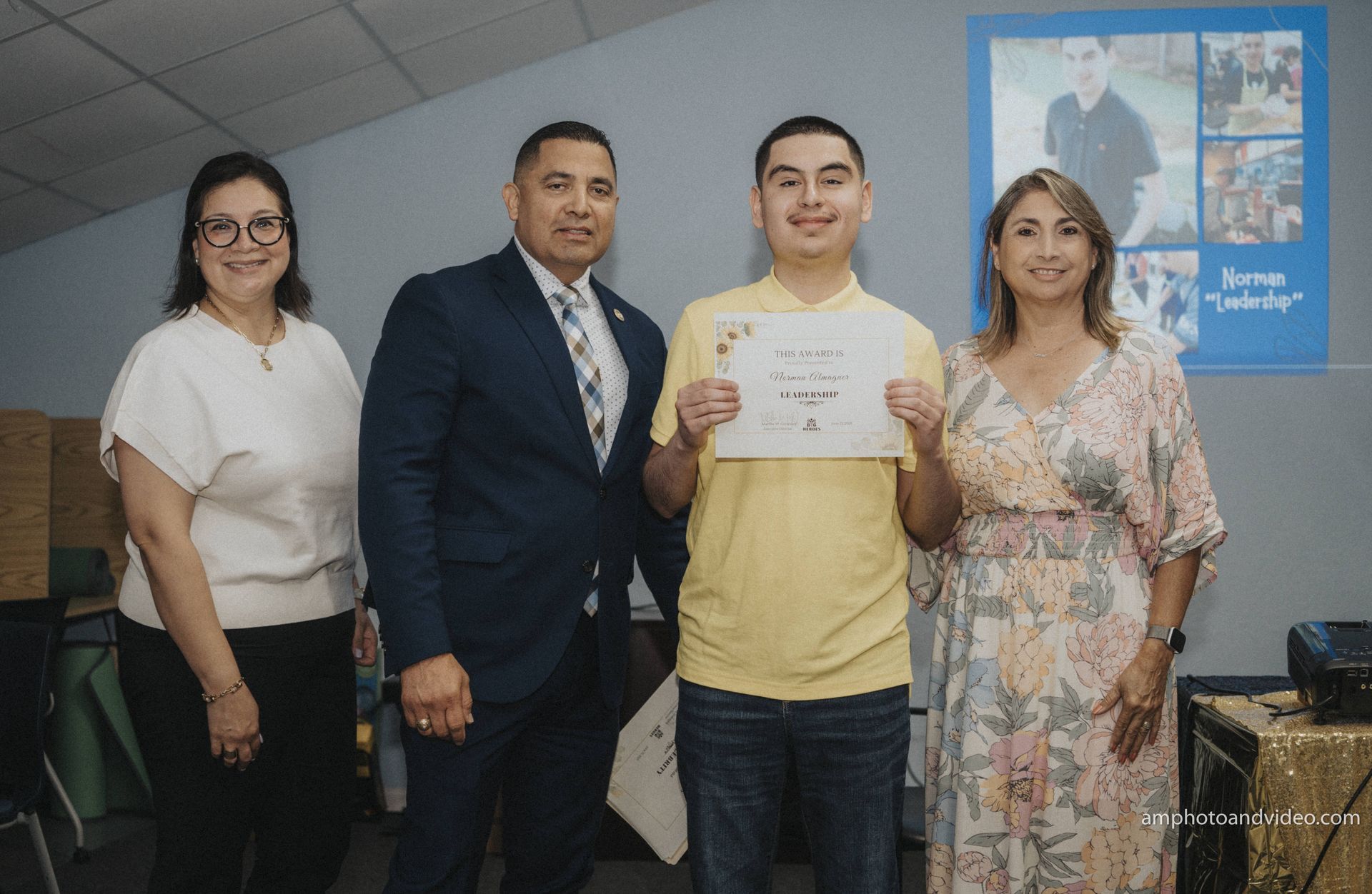 Four people posing for photo, holding certificate, indoors with blue poster in background.