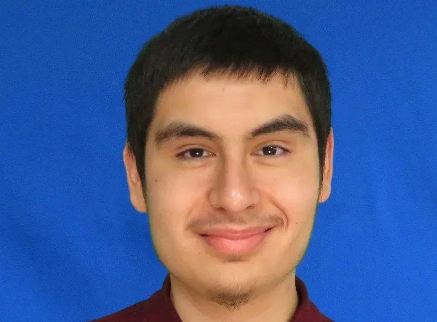A young man in a red shirt is smiling in front of a blue background.