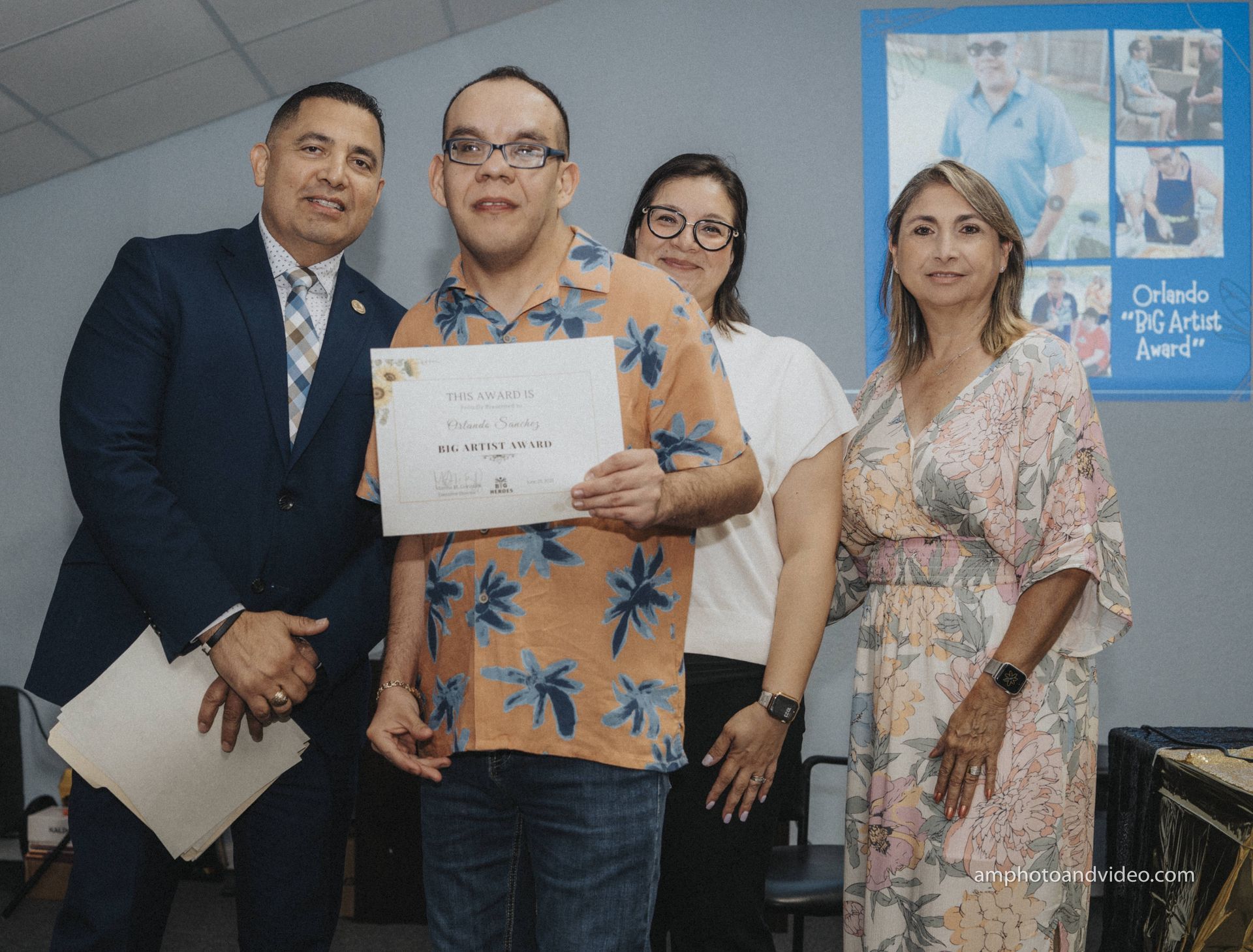 Four people pose; a man with glasses holds an award, flanked by two women and a man in a suit.
