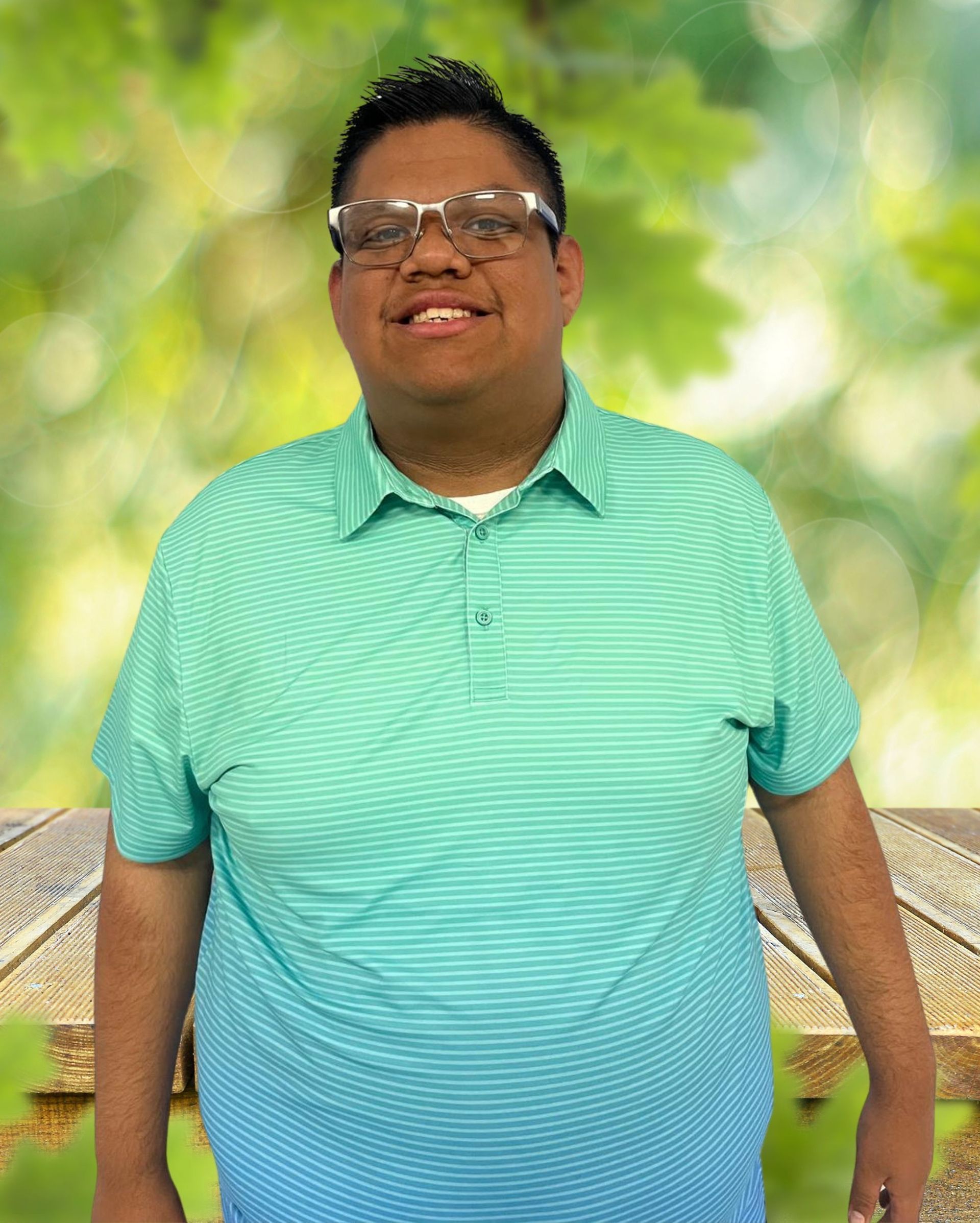 A man wearing glasses and a green shirt is standing in front of a wooden table.