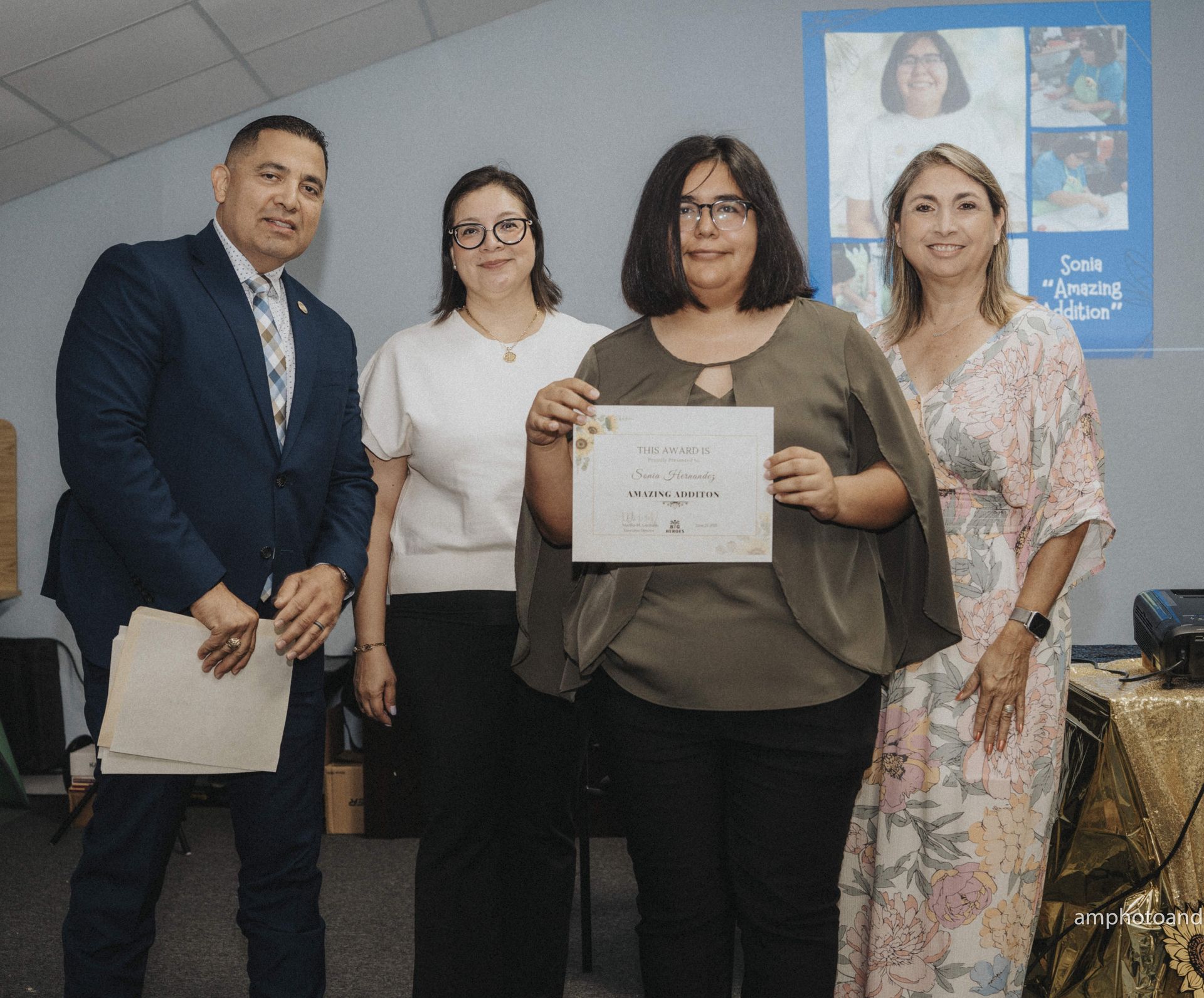 Group of four people; woman holding a certificate, smiling, in front of a banner.