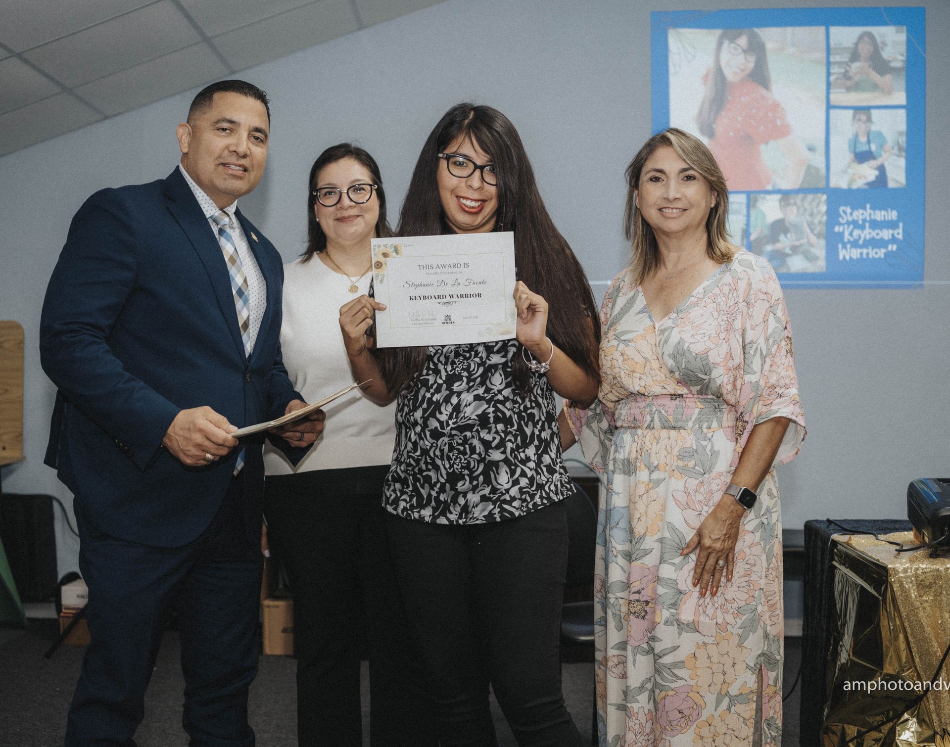 Four people at an event, one holding a certificate. They are in a room with a poster.