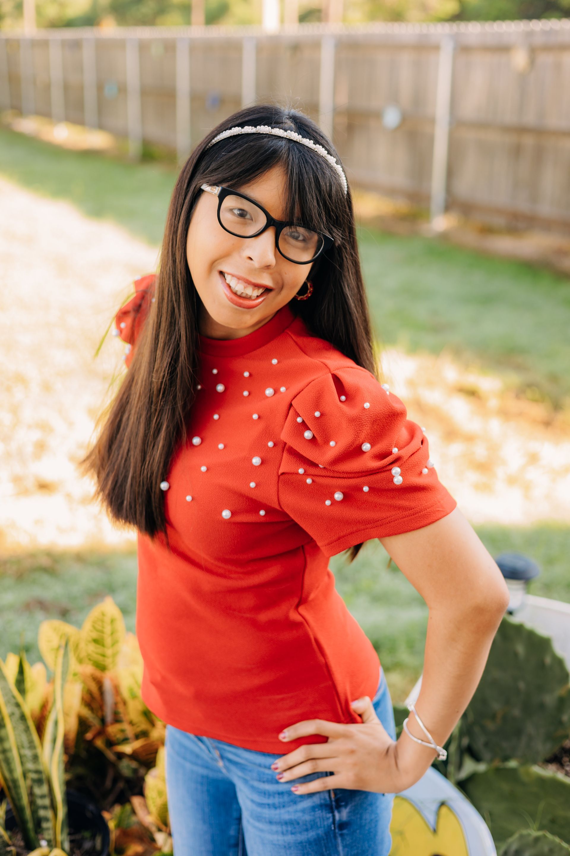 A woman wearing glasses and a red shirt is standing with her hands on her hips.