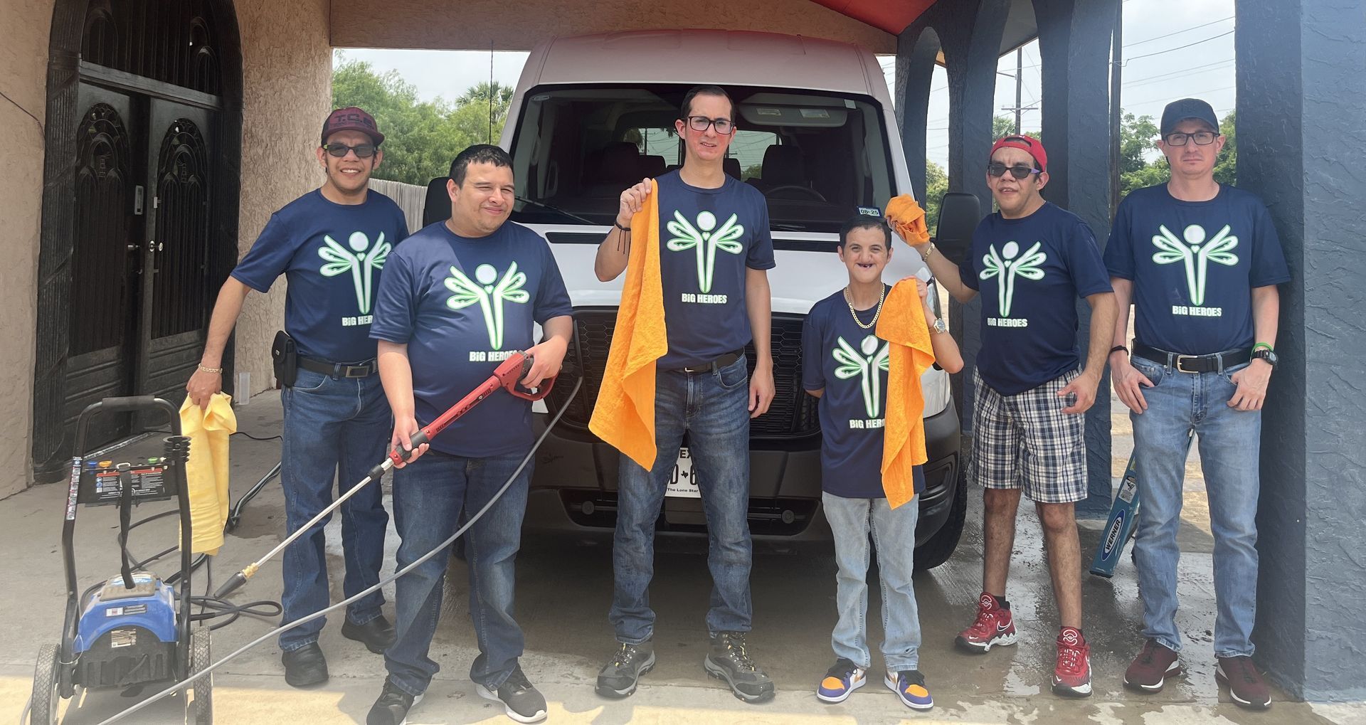 A group of people standing in front of a van wearing blue shirts with palm trees on them