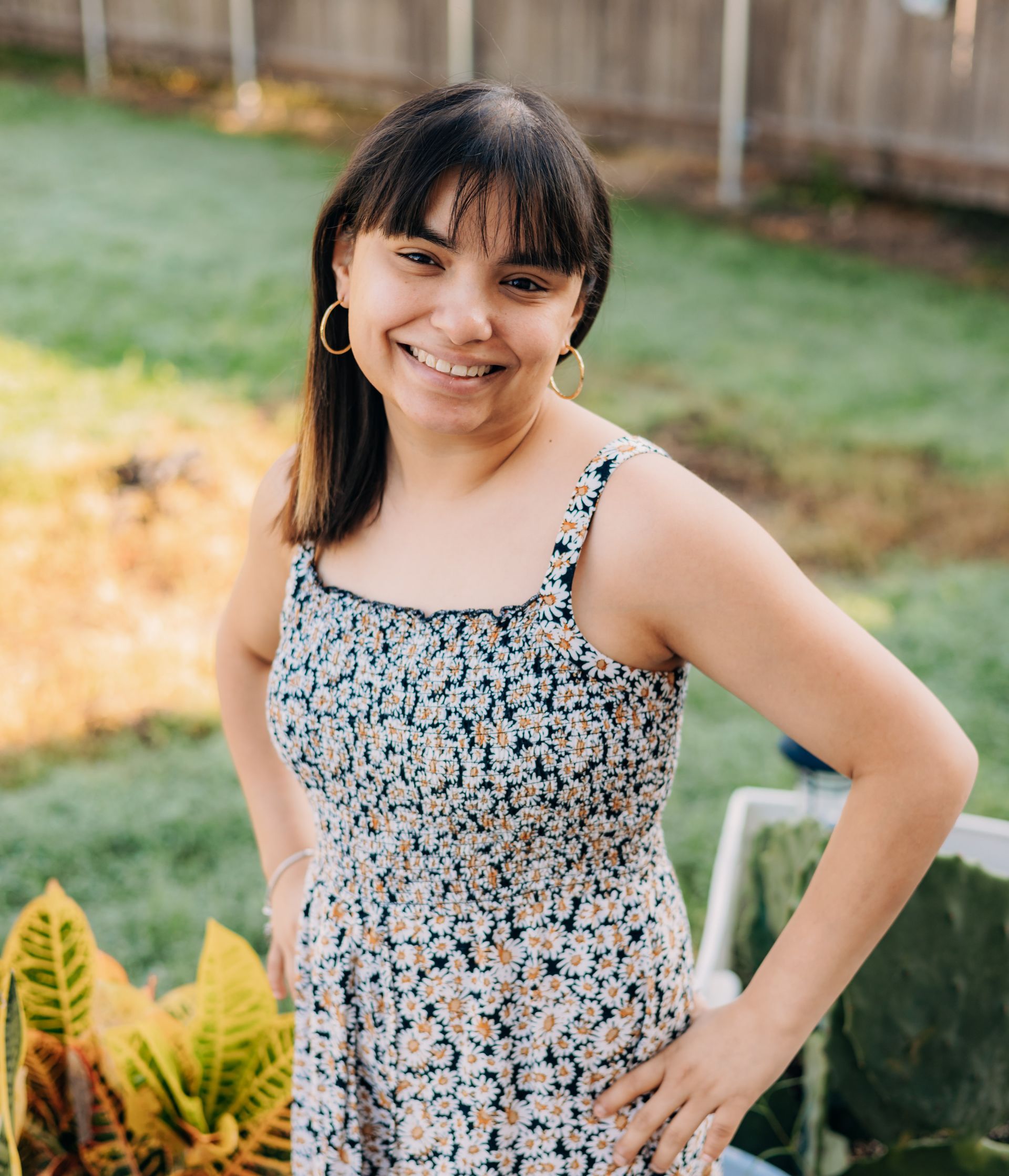 A woman in a floral dress is standing in the grass with her hands on her hips.