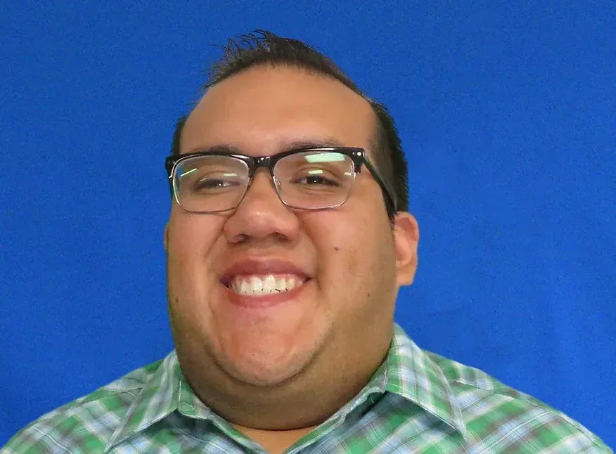 A man wearing glasses and a plaid shirt is smiling.