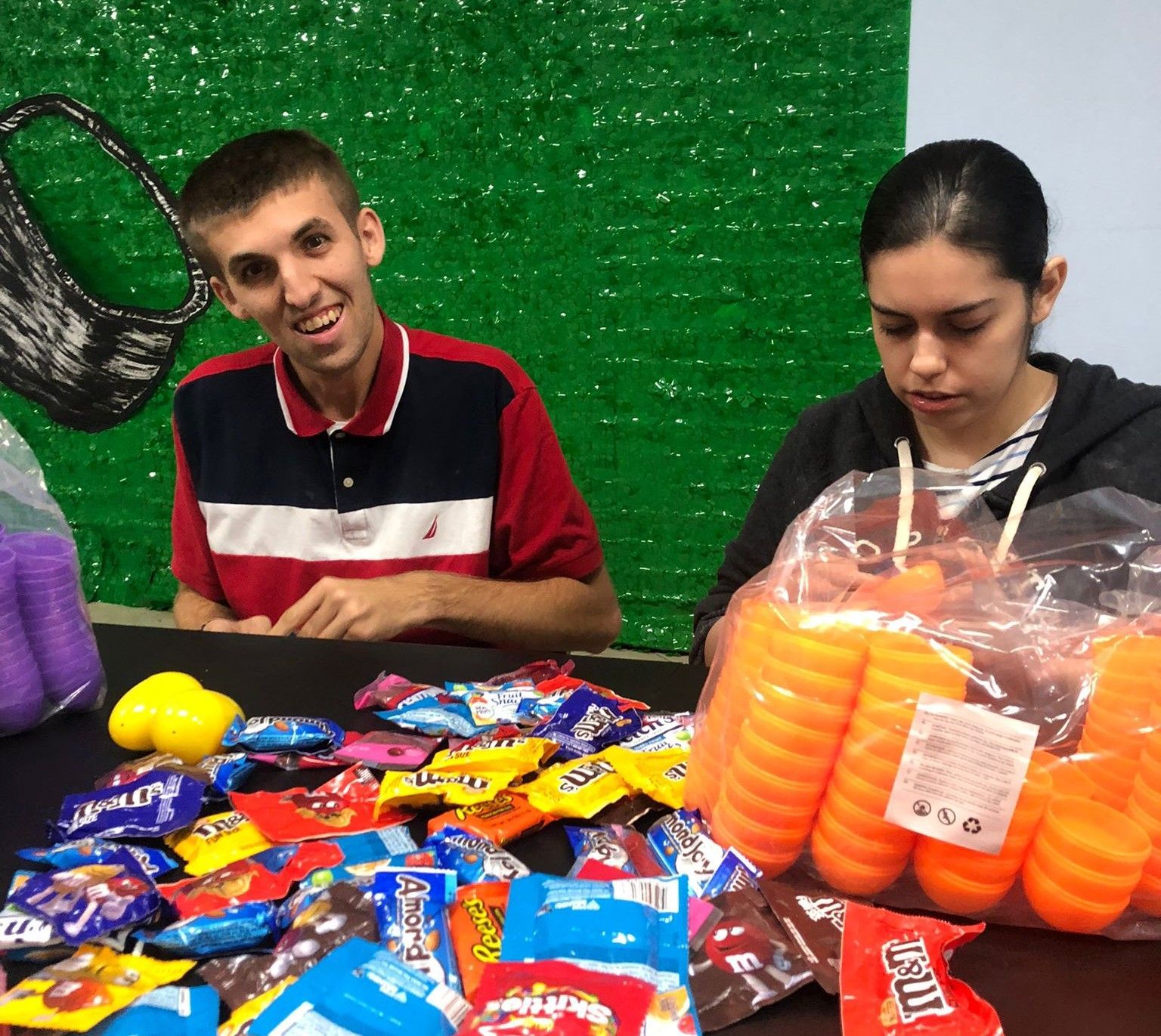 A man and a woman are sitting at a table with a bunch of candy on it.