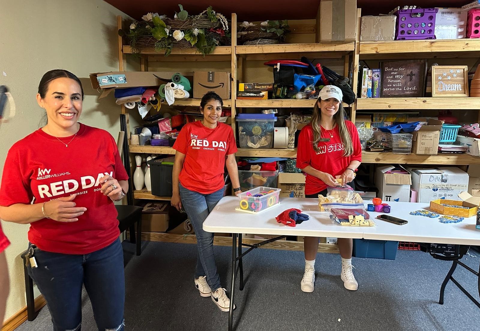 Three women in red shirts are standing around a table in a room.