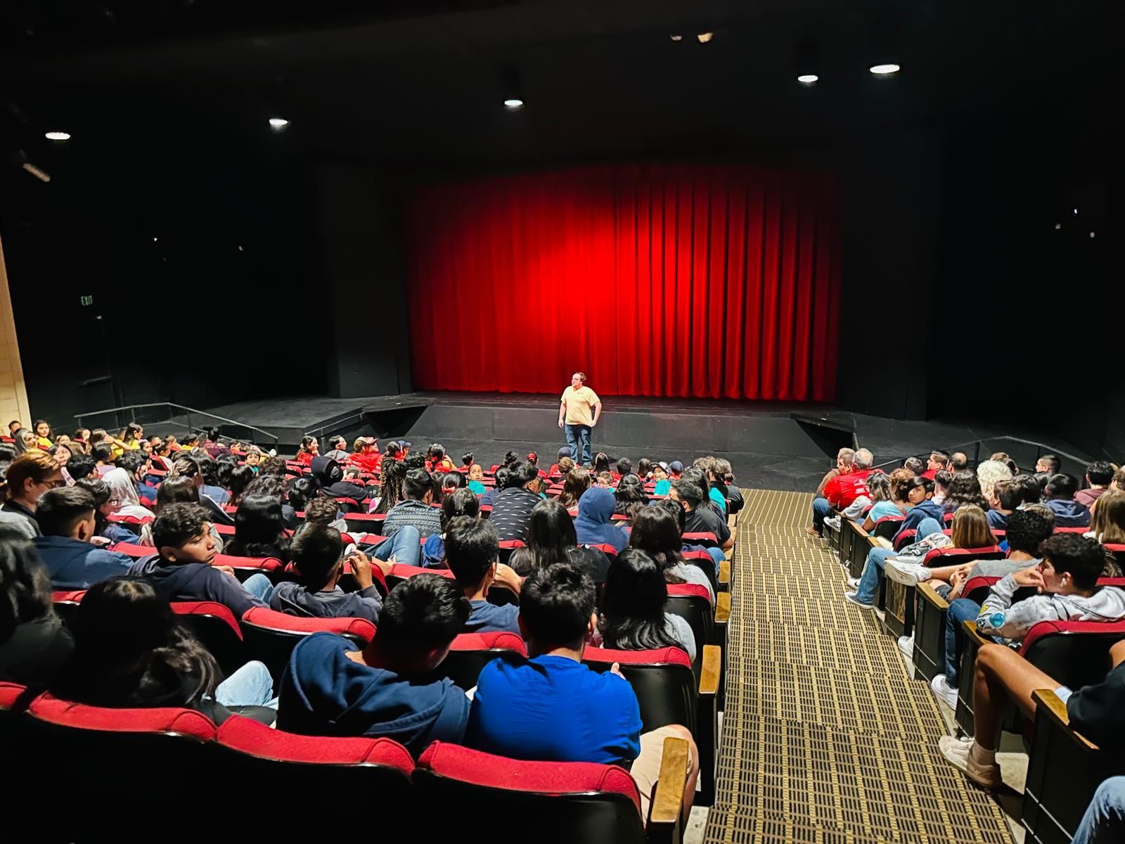 A man is standing on a stage in front of a crowd of people in an auditorium.
