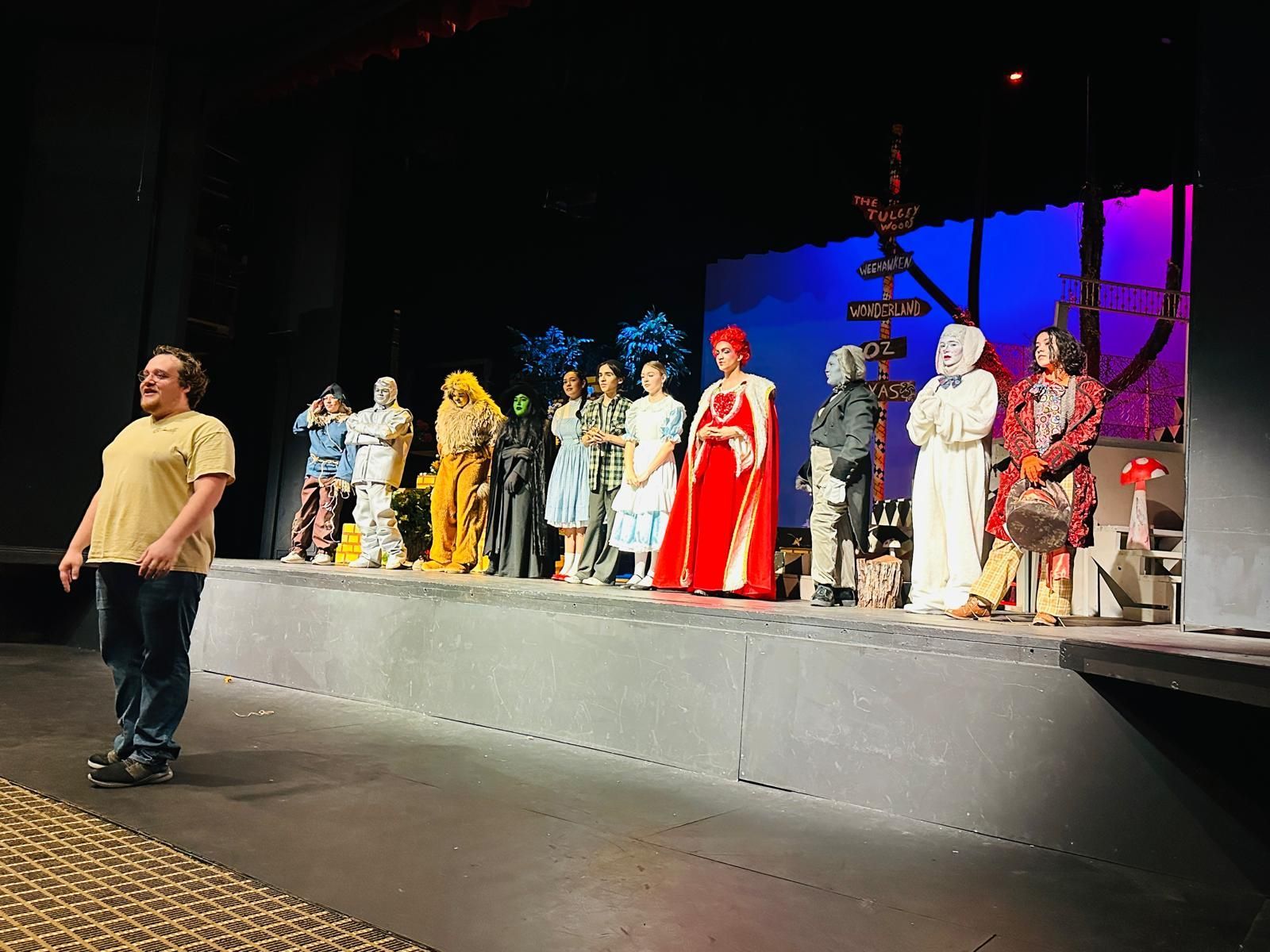 A man is standing on a stage next to a group of people in costumes.