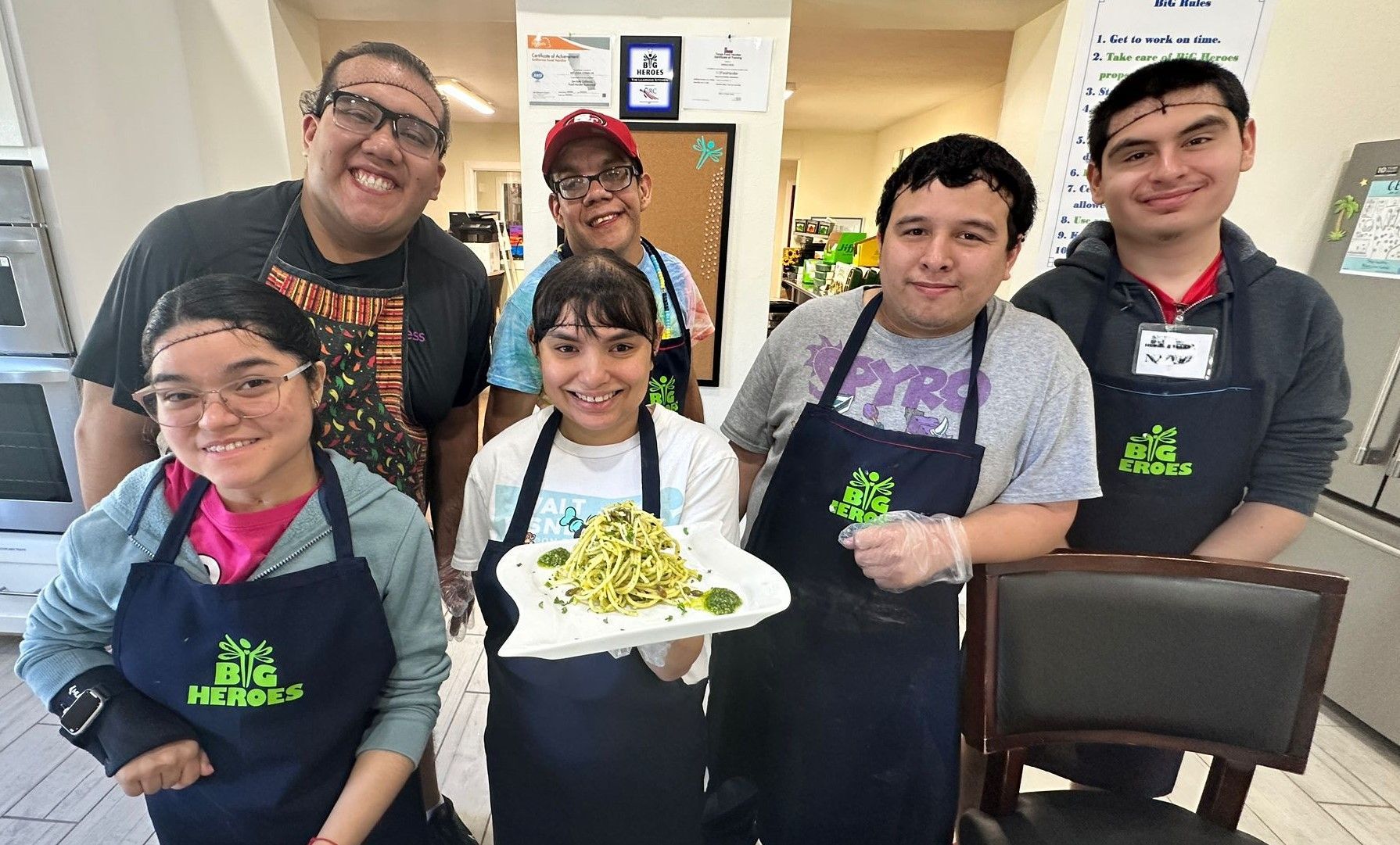 A group of people wearing aprons are standing in a kitchen holding a plate of food.