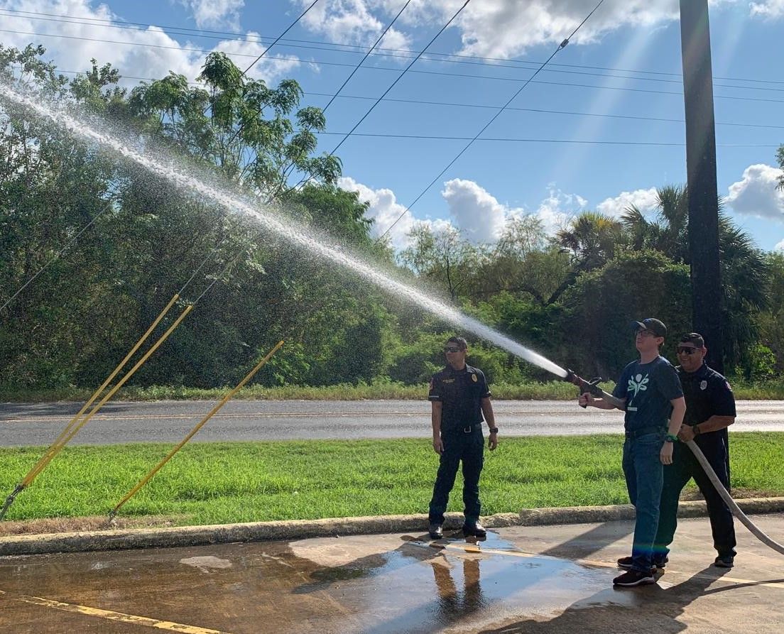 Two men are spraying water from a fire hose in a parking lot.