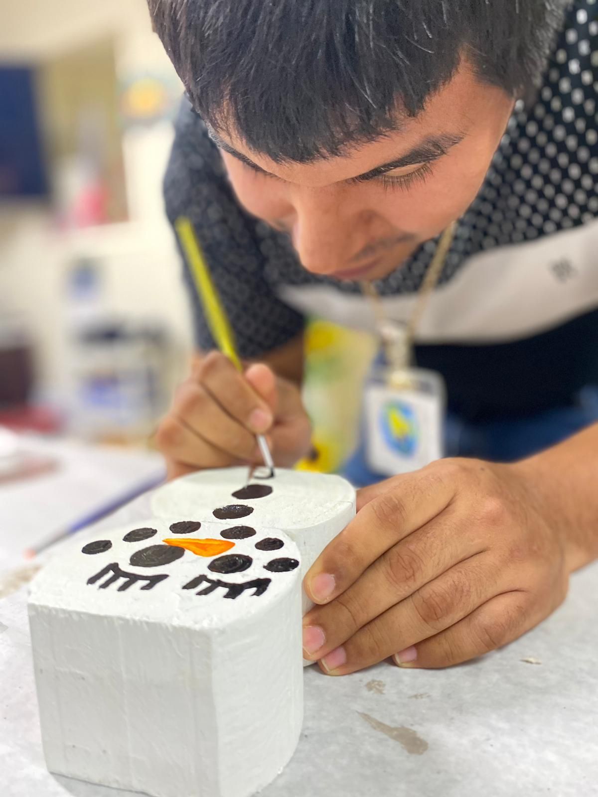 A man is painting a snowman on a white block