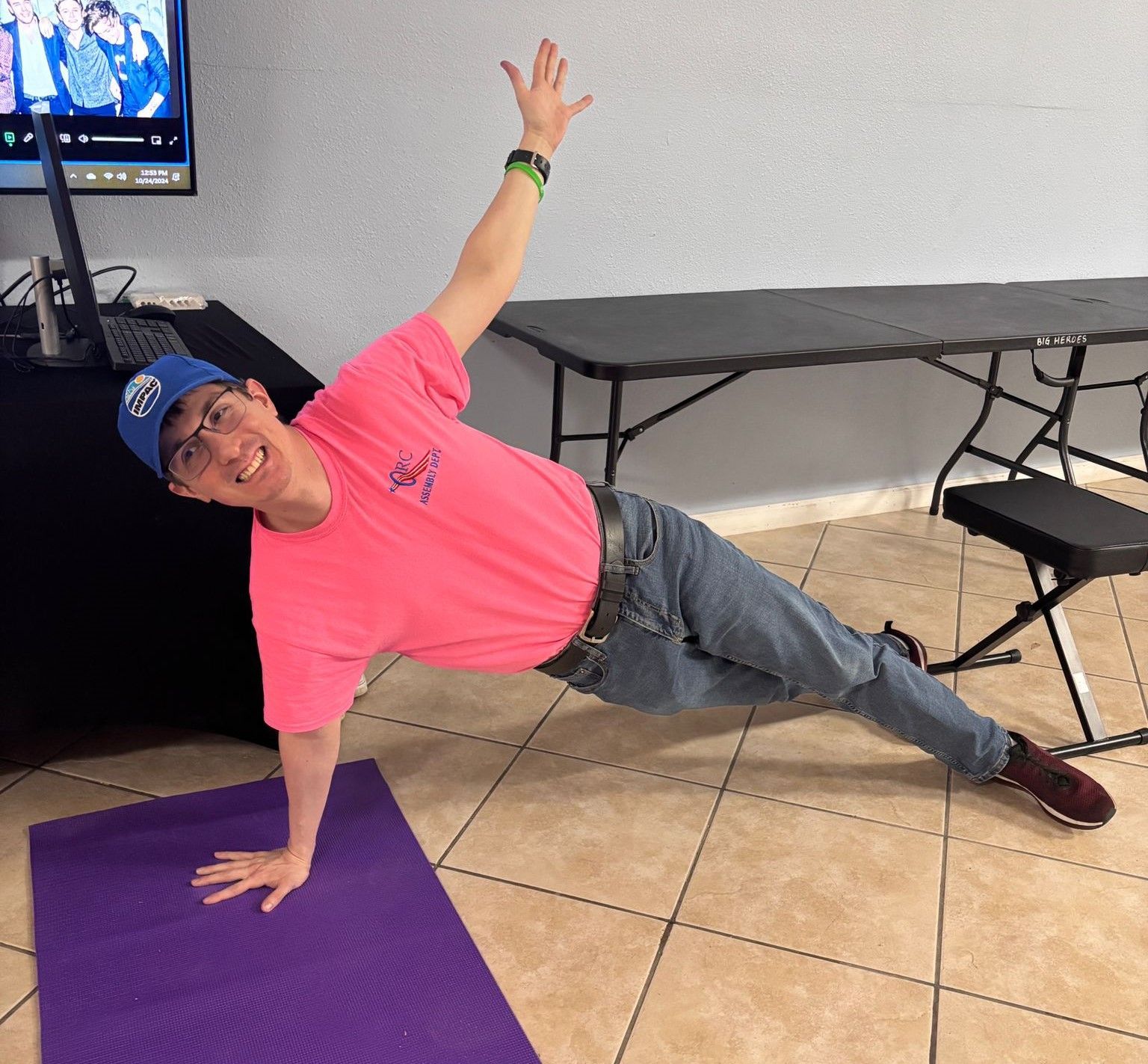 A man in a pink shirt is doing a plank on a purple mat