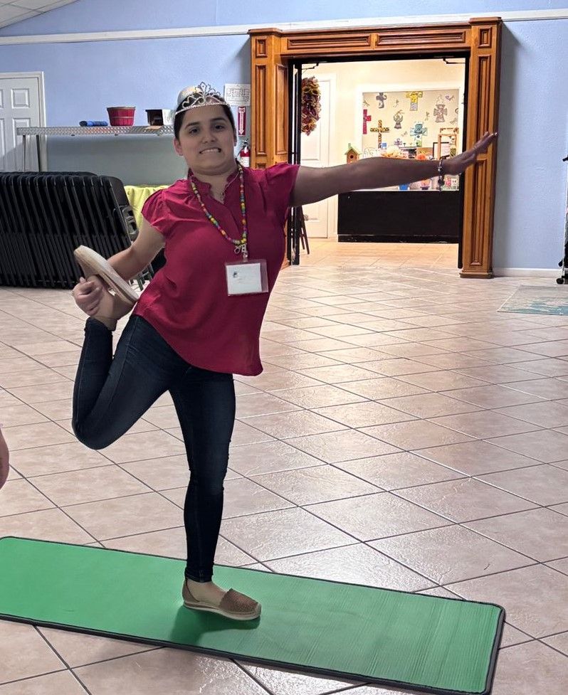A woman is standing on one leg on a yoga mat