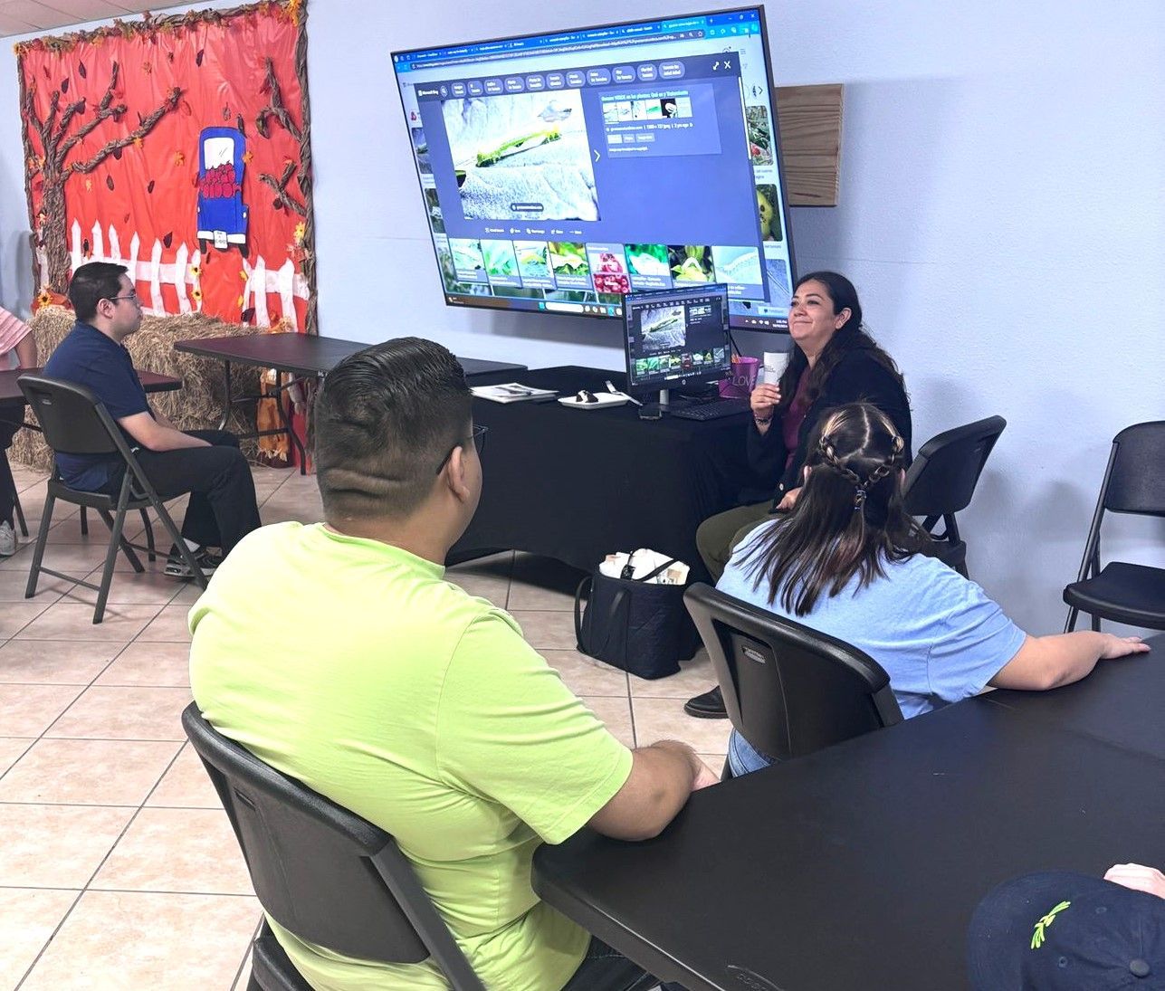 A group of people are sitting at tables in front of a large screen.