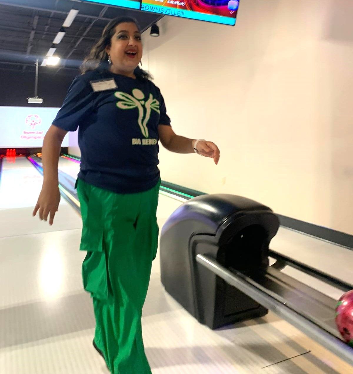 A woman in a bowling alley wearing green pants and a blue shirt