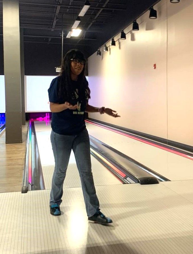 A woman is standing on a bowling alley holding a bowling ball.