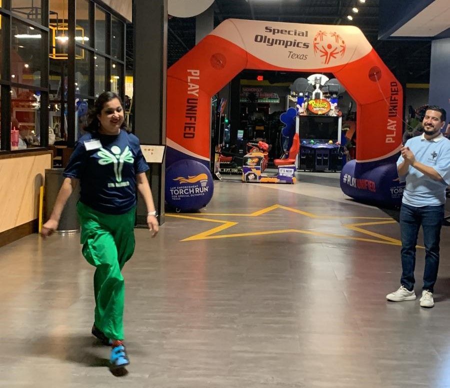 A woman in green pants is walking under an inflatable arch that says play united