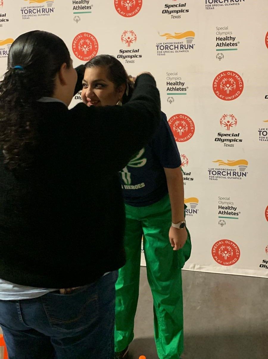 Two women hugging each other in front of a wall that says torchman